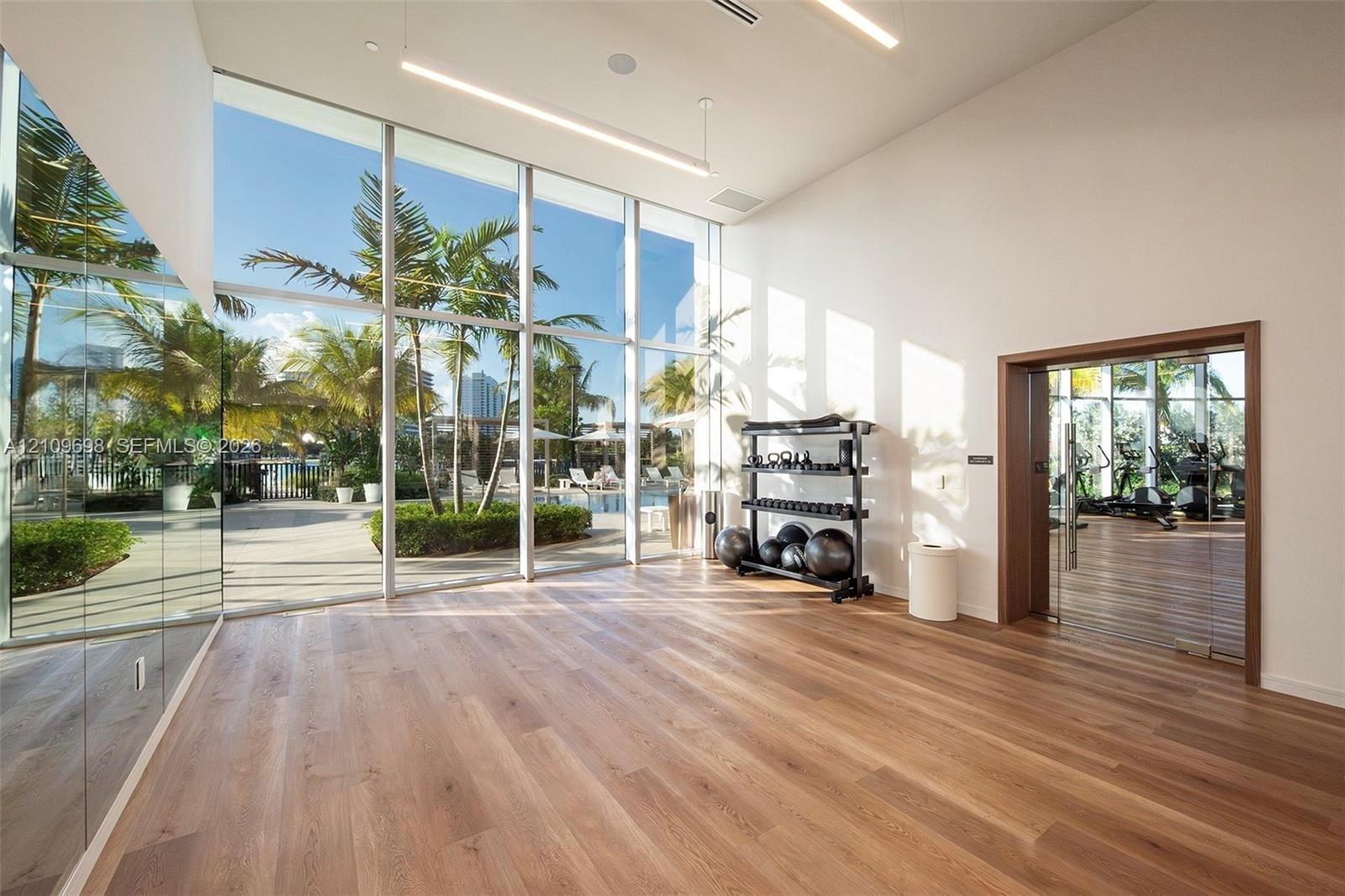 Floor-to-ceiling windows, wood-finish flooring, full-wall mirrors, recessed linear lighting, and glass-paneled entry door