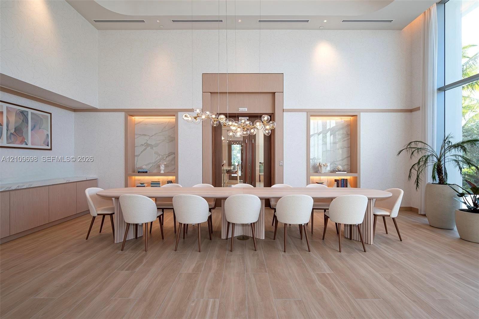 High-ceilinged room featuring wood-finish flooring, dual built-in shelving niches with stone-slab backsplashes, custom millwork, and an intricate multi-globe chandelier