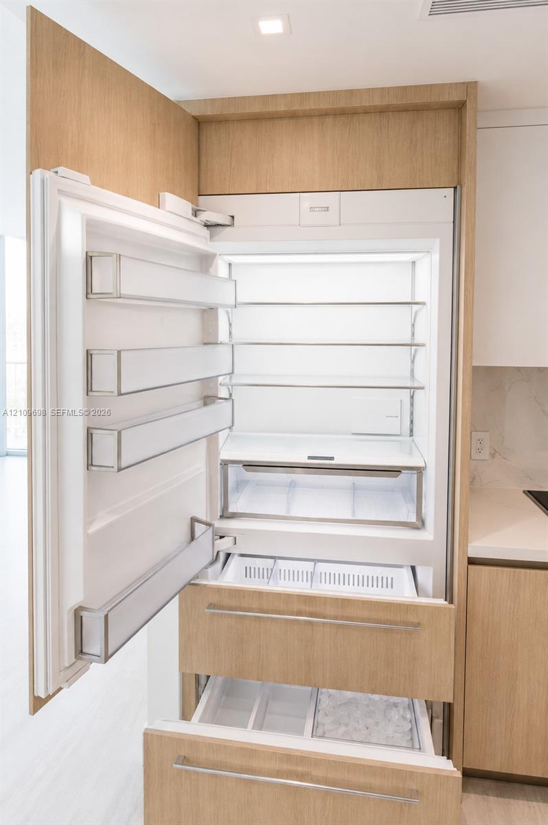 Integrated refrigerator featuring custom wood-finish cabinetry panels, adjustable shelving, tiered pull-out freezer drawers, and recessed lighting