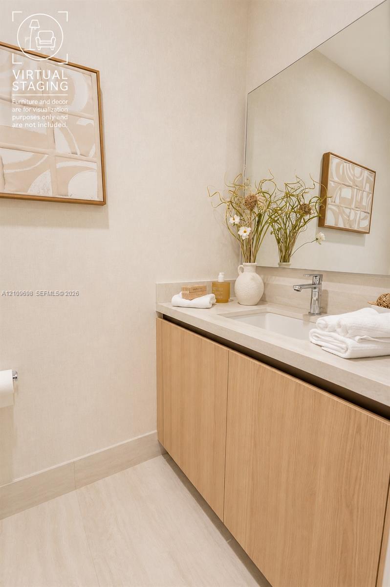 Floating vanity with light wood-finish cabinetry, stone-style countertop, integrated sink, chrome faucet, and expansive frameless wall mirror