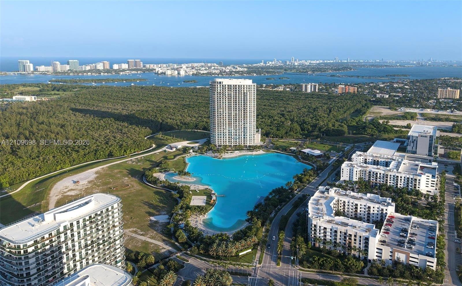 Aerial perspective featuring a high-rise residential structure, a large-scale lagoon-style water feature, and expansive green space with mature trees