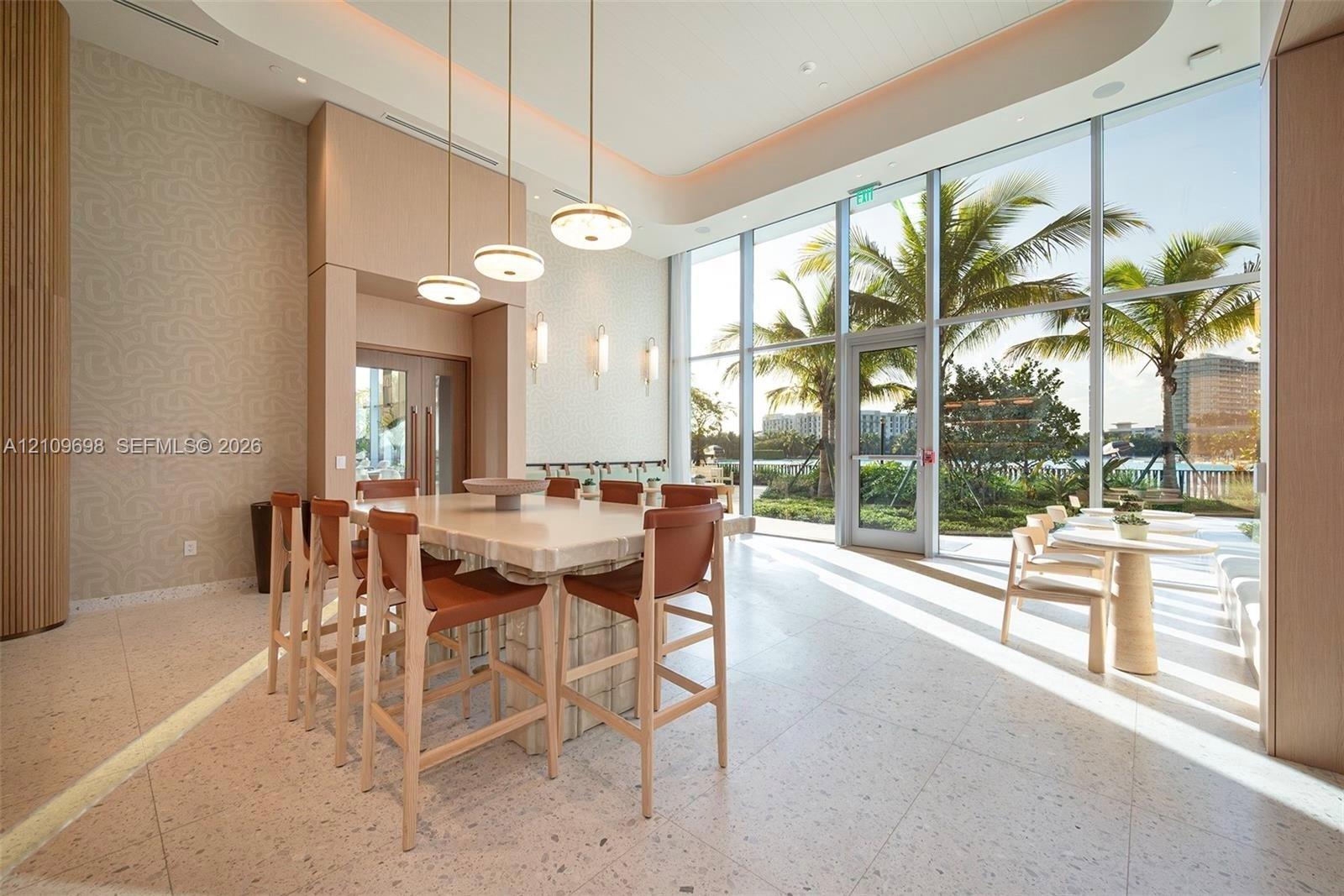 Floor-to-ceiling windows, stone-finish tile flooring, recessed tray ceiling, pendant lighting, and a built-in stone island