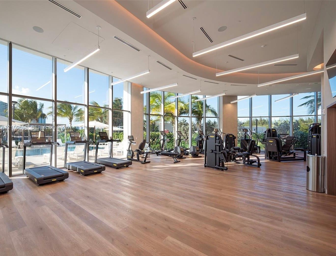 Fitness facility featuring floor-to-ceiling windows, wood-finish flooring, curved architectural ceiling detail, and recessed linear lighting