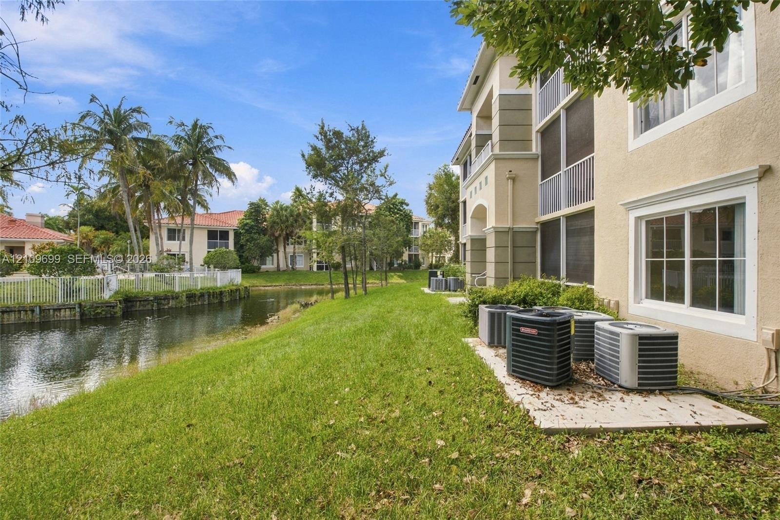 Multi-story stucco exterior featuring screened balconies, multi-pane windows, and a canal-front setting with landscaped grounds