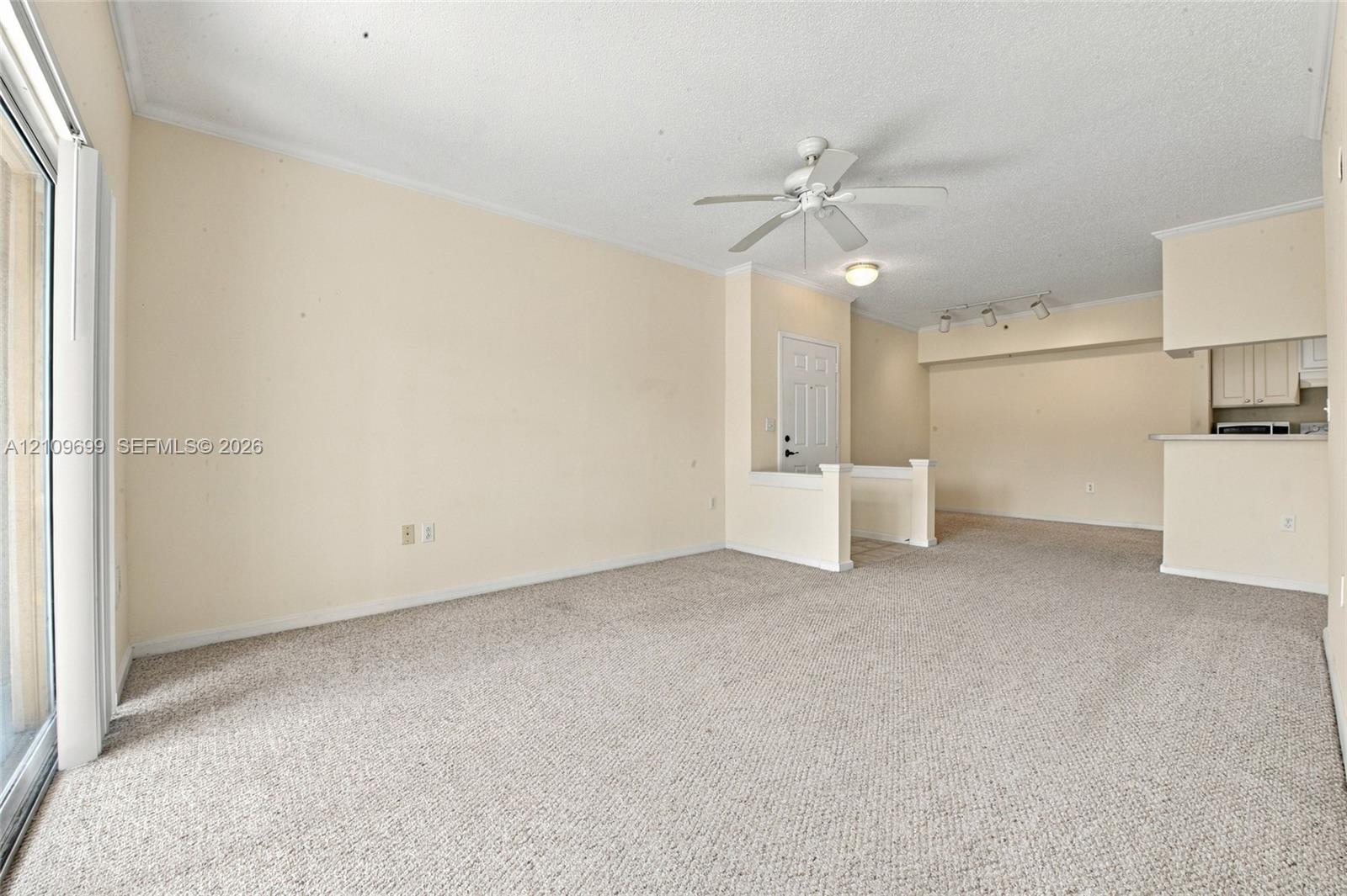 Interior space featuring neutral carpeting, a ceiling fan with integrated lighting, track lighting, and a sliding glass door