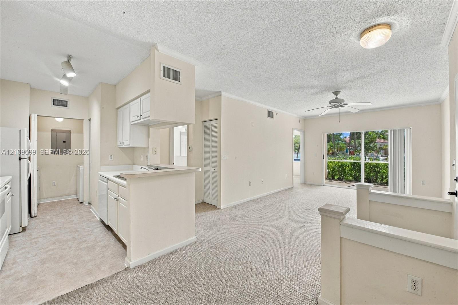 Open-concept interior featuring wall-to-wall carpeting, a kitchen with white cabinetry and a breakfast bar, a ceiling fan with integrated lighting, and sliding glass doors providing natural illumination