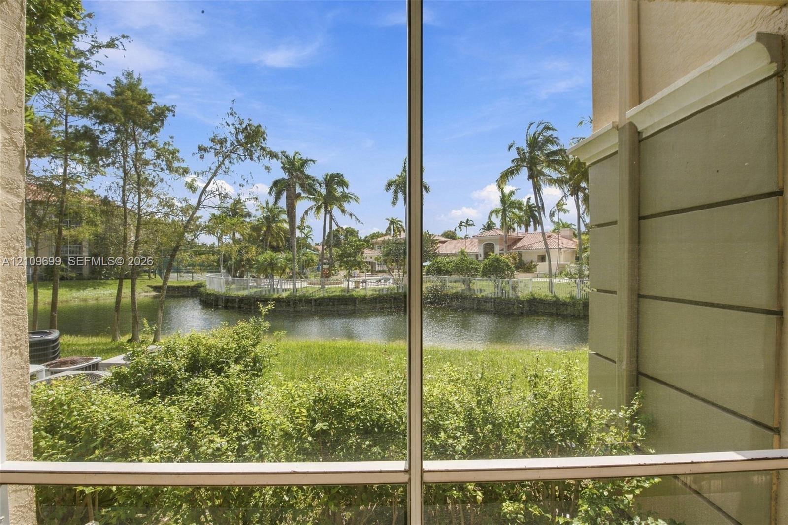 Screen-enclosed outdoor space featuring a water pond, lush landscaping, and palm trees