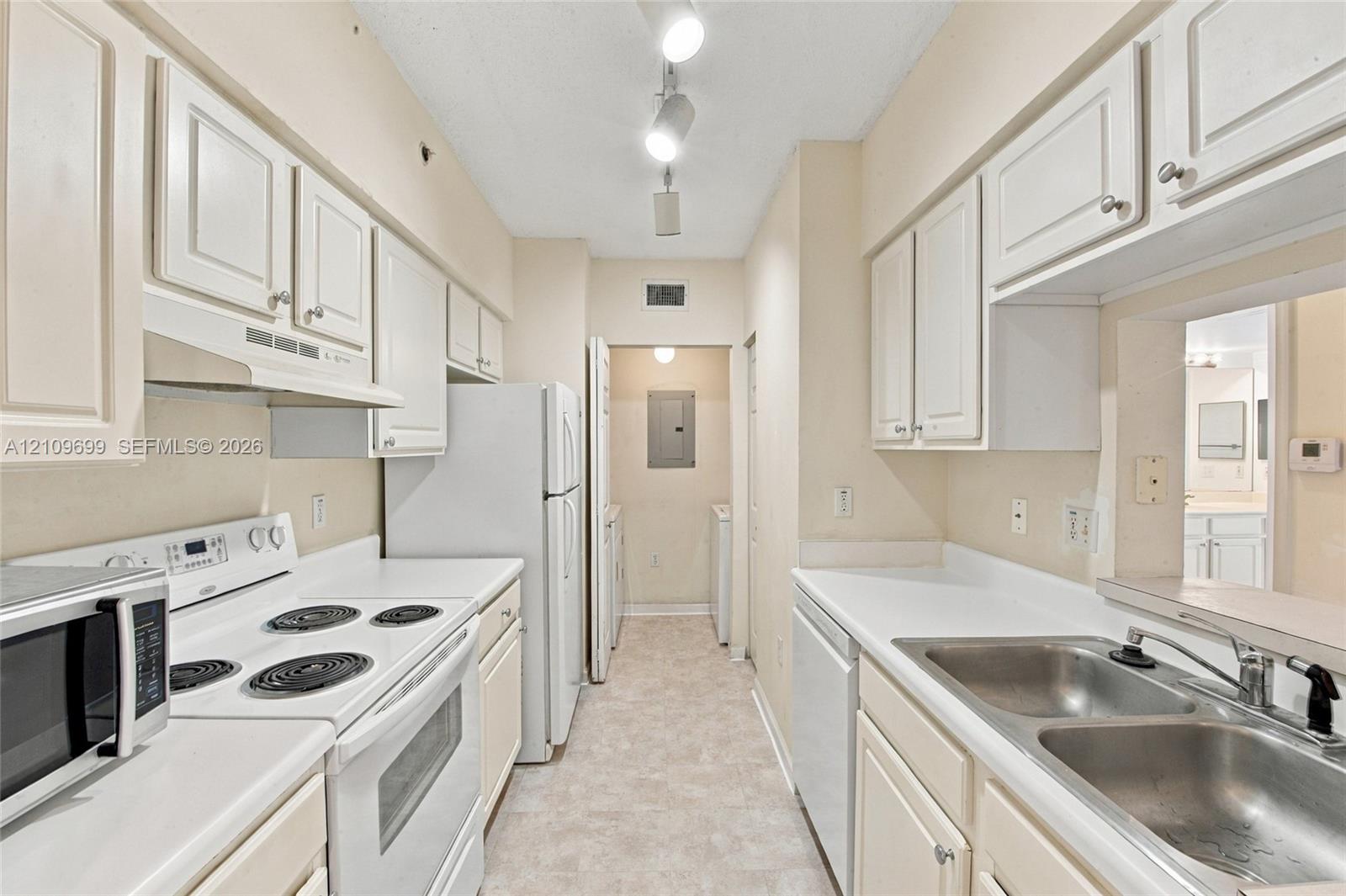 Galley kitchen featuring white cabinetry, solid-surface countertops, dual-basin stainless steel sink, and track lighting