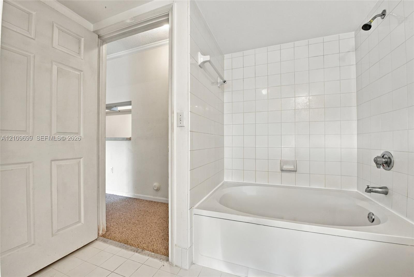 Bathroom featuring a white bathtub, ceramic tile shower surround, chrome plumbing fixtures, and a four-panel interior door