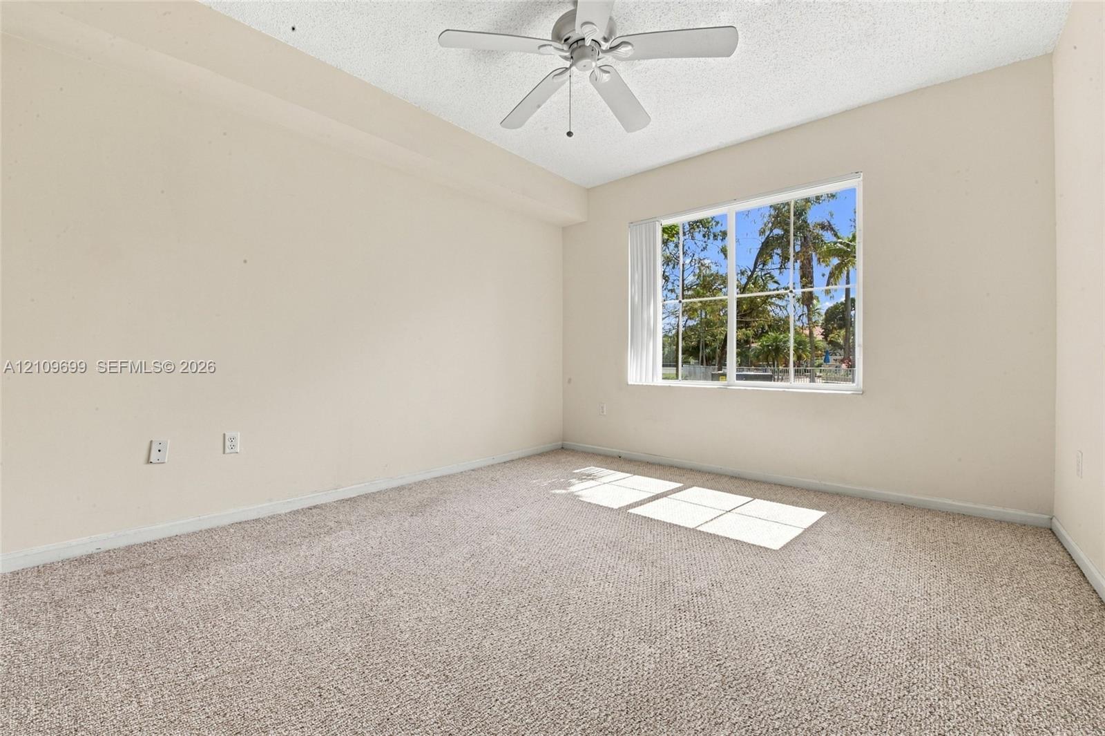 Interior room featuring neutral wall paint, wall-to-wall carpeting, a ceiling fan with integrated light fixture, and a large multi-pane window with vertical blinds