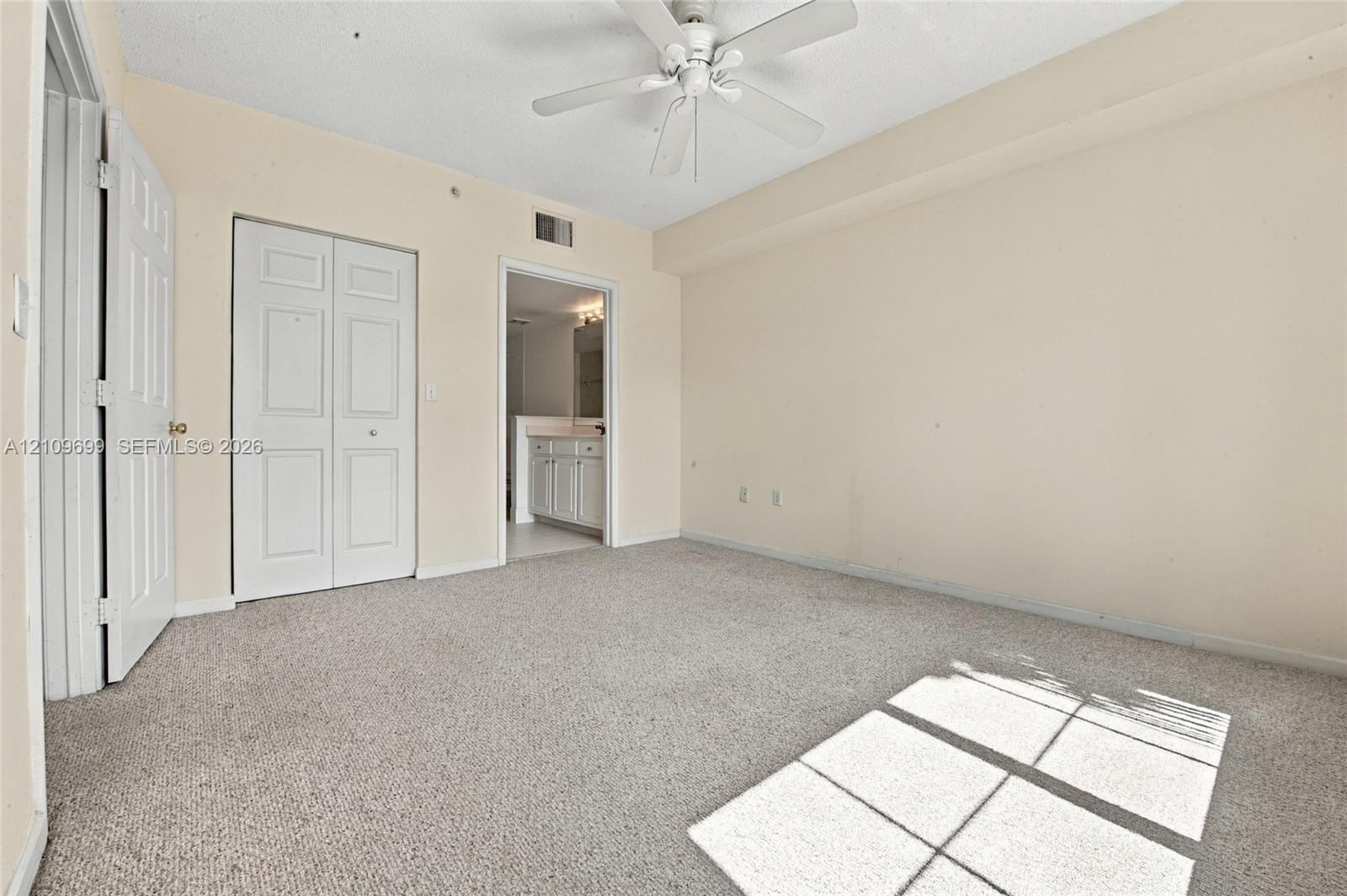 Neutral-toned room featuring neutral carpeting, a ceiling fan, and double-door closet storage