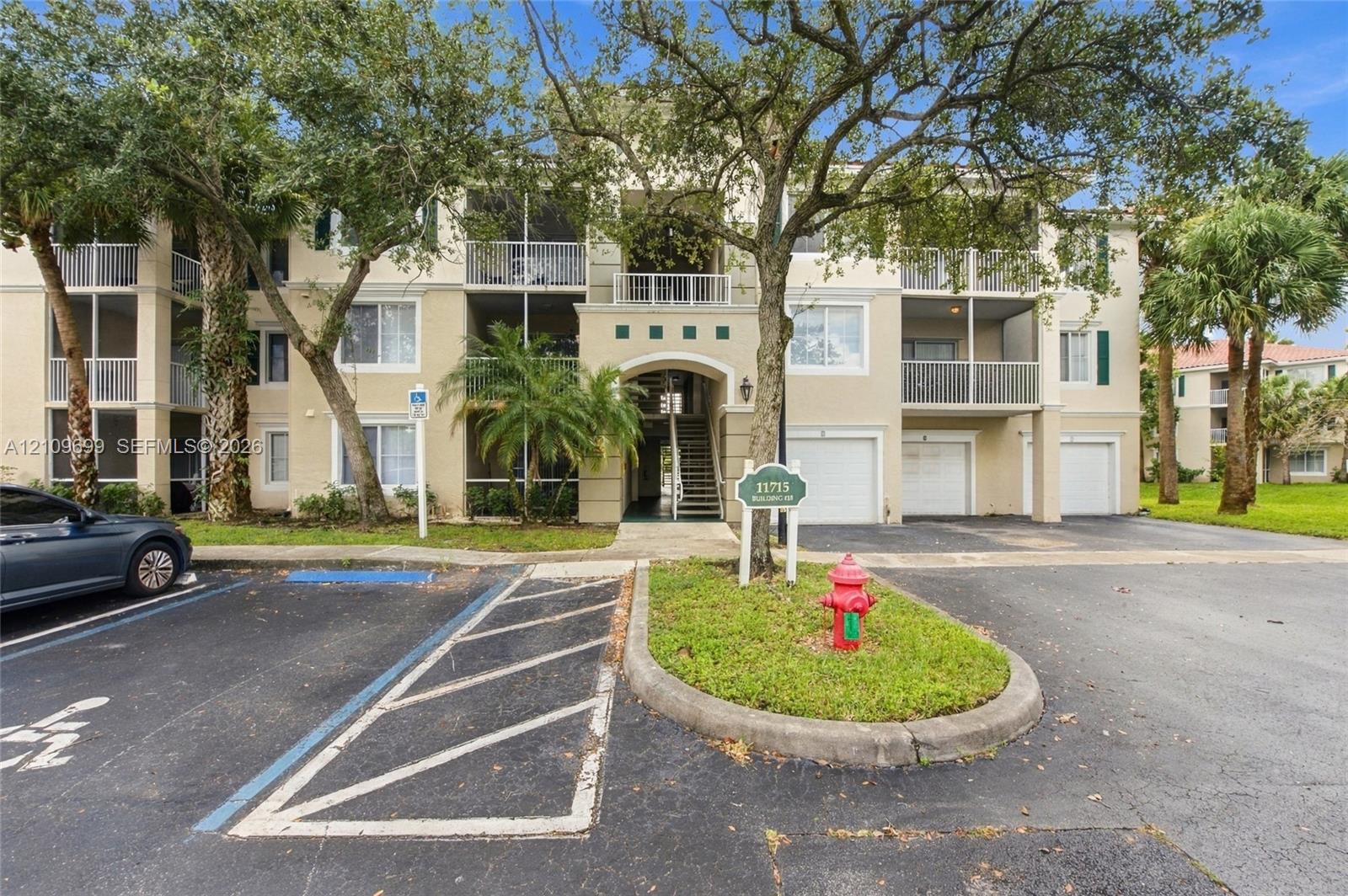 Multi-level building exterior featuring private balconies, attached garages, and exterior stair access amidst established landscaping