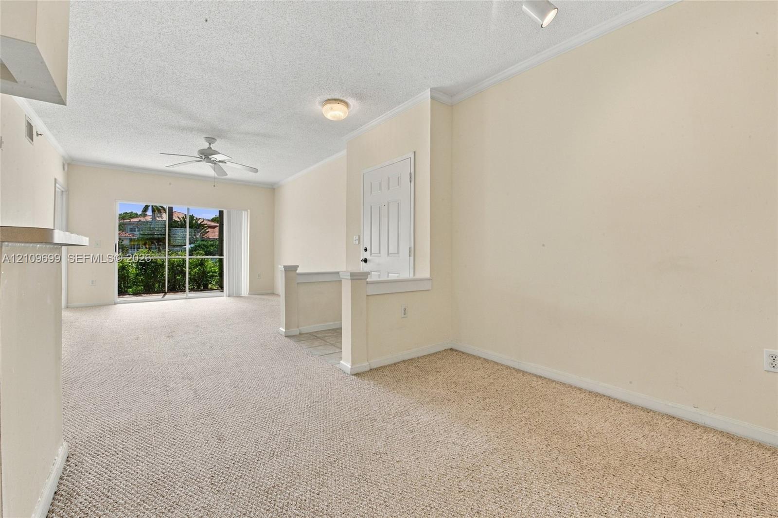 Interior space featuring carpeted flooring, a ceiling fan, crown molding, and sliding glass doors providing outdoor access