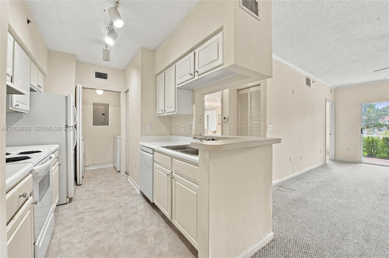 Kitchen featuring white cabinetry, solid-surface countertops, dual-basin stainless steel sink, track lighting, and white appliances