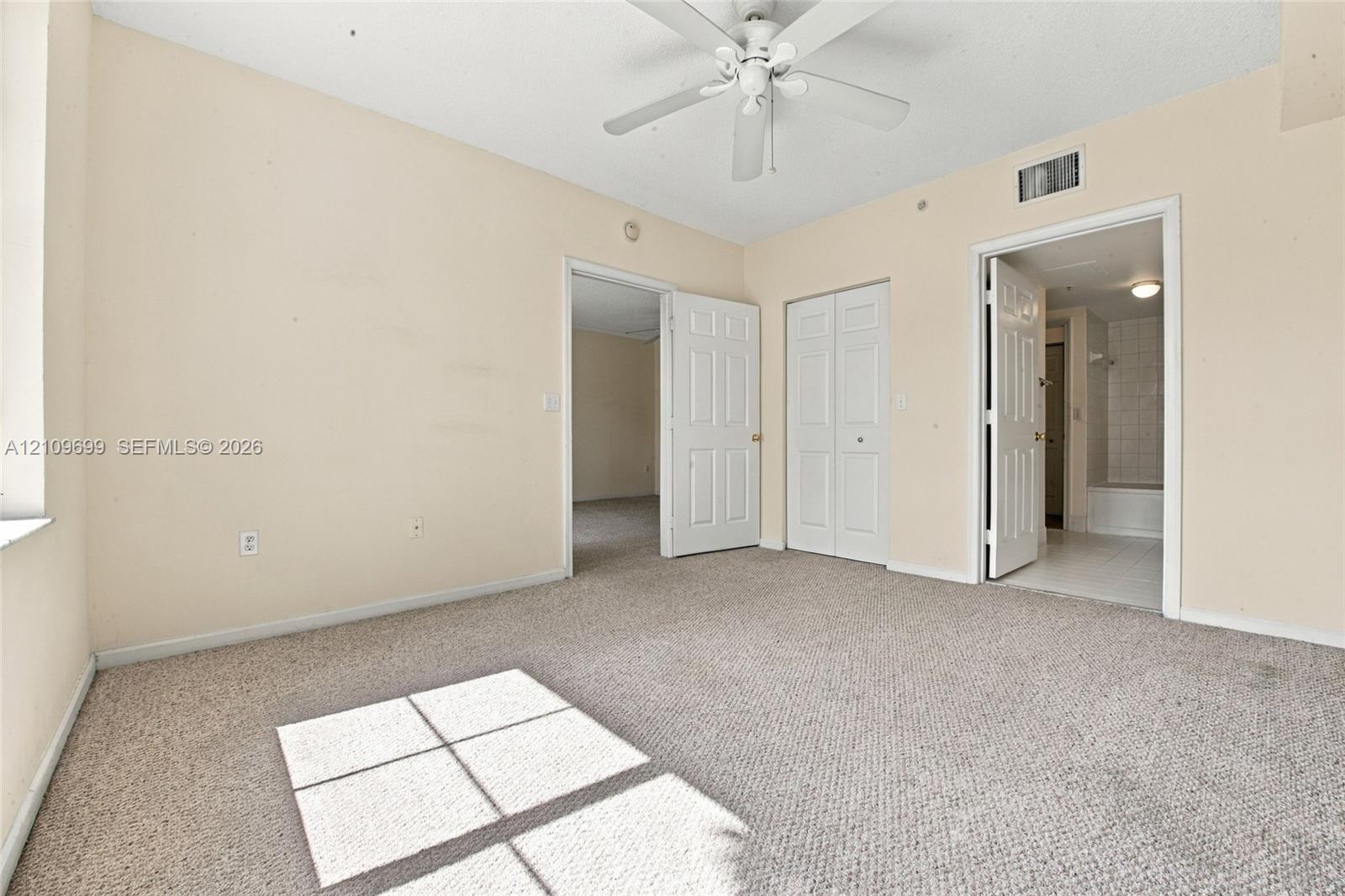 Neutral-toned room featuring wall-to-wall carpeting, a white ceiling fan with integrated lighting, dual-panel interior doors, and a double-door closet