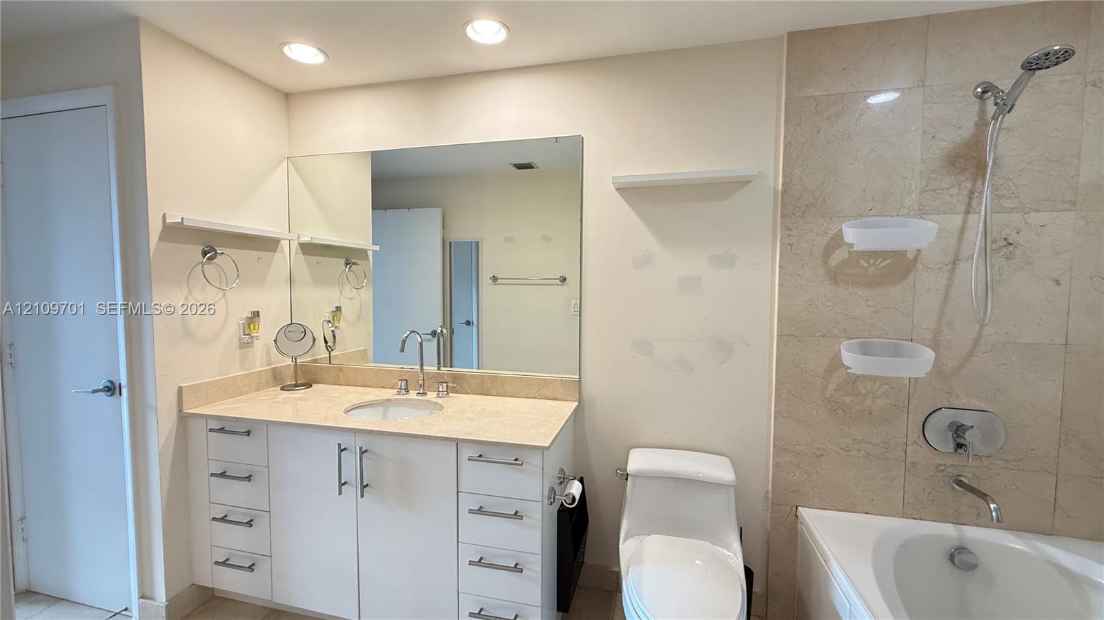 Bathroom featuring a white vanity with drawers, stone-surfaced countertop, large wall-mounted mirror, recessed lighting, and a bathtub with tile surround