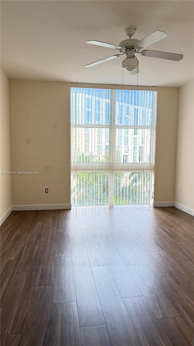 Floor-to-ceiling windows with vertical blinds, wood-finish flooring, and a central ceiling fan