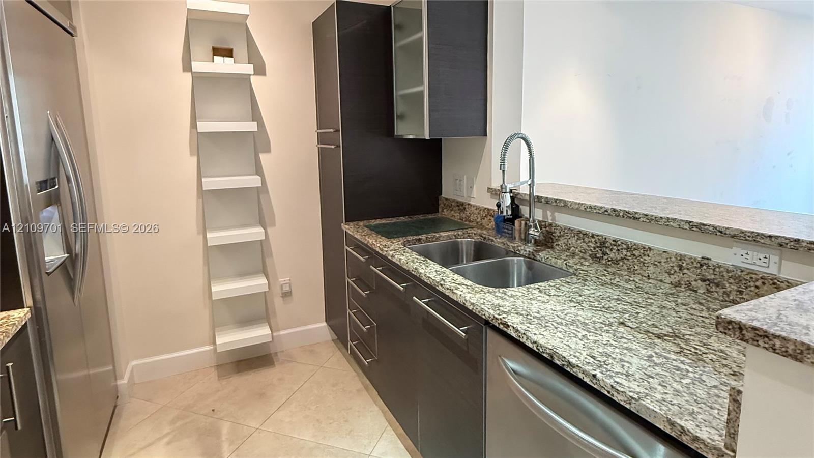Kitchen featuring stone countertops, stainless steel appliances, dark cabinetry, tile flooring, and integrated shelving Kitchen featuring stone countertops, stainless steel appliances, dark cabinetry, tile flooring, and integrated shelving
