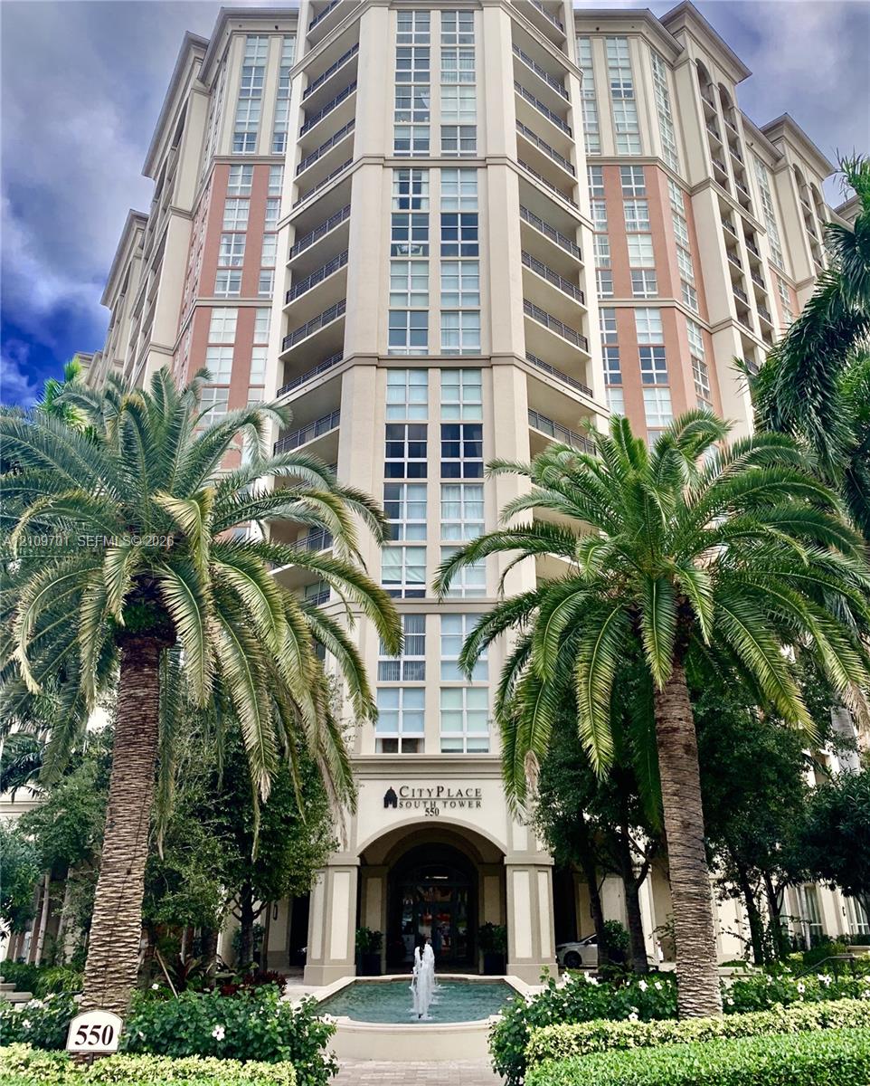 Multi-story high-rise exterior featuring a symmetrical facade, vertical glass paneling, recessed balconies, a formal arched entryway, and a tiered decorative fountain