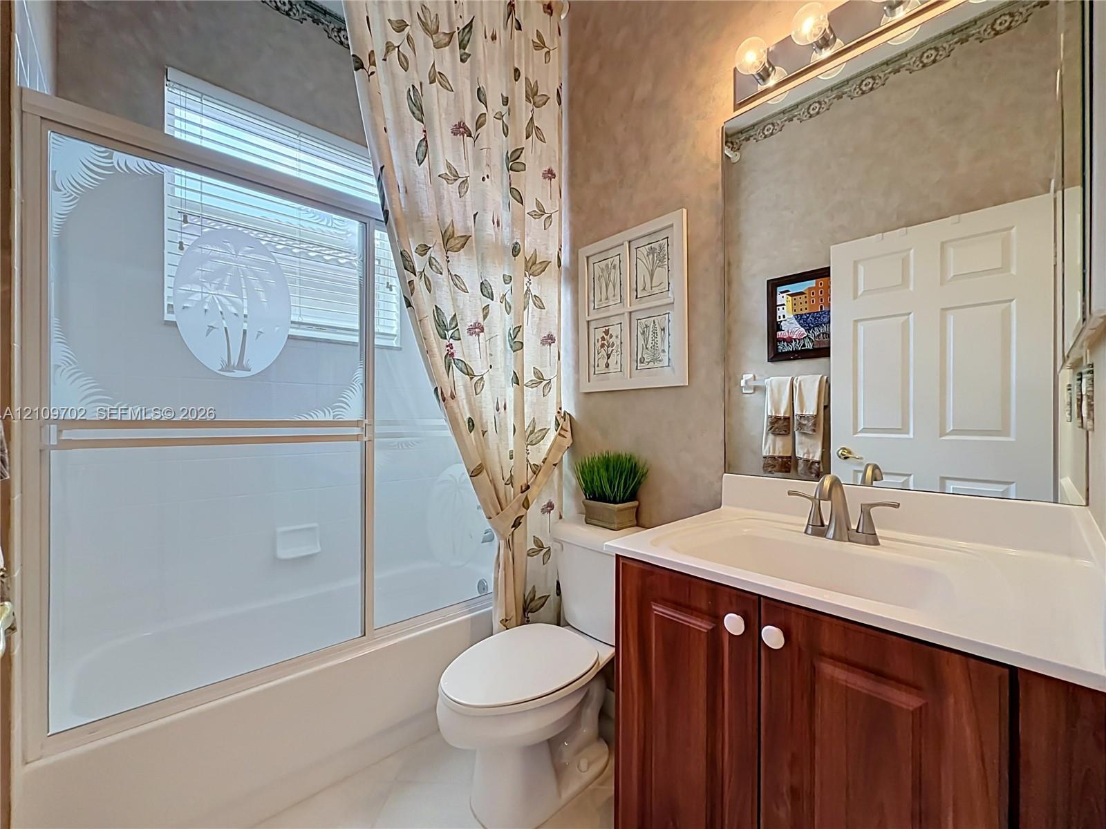 Bathroom featuring a wood-finish vanity with a white countertop, large wall-mounted mirror, glass-enclosed shower with decorative etched detailing, and integrated lighting