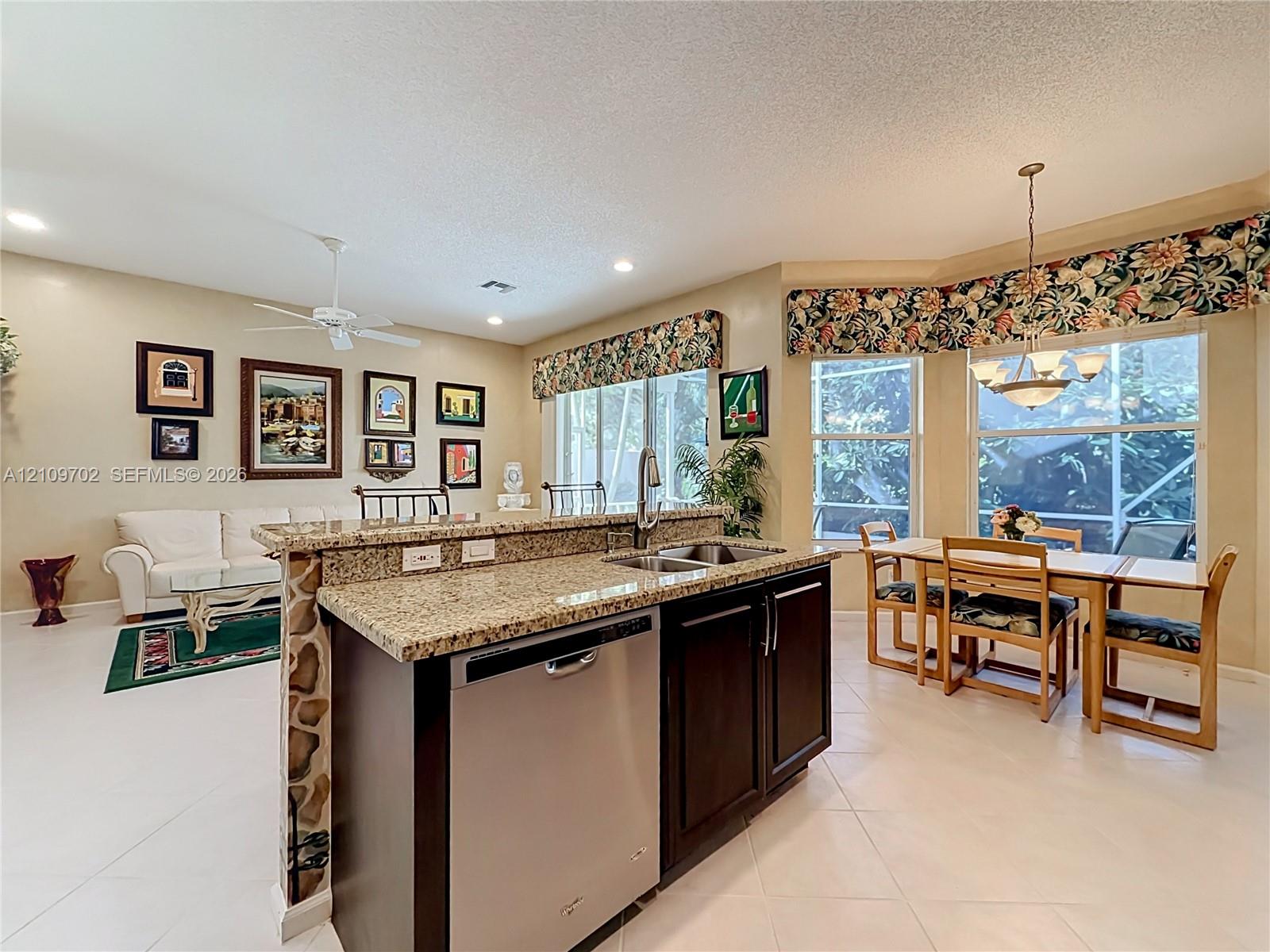 Kitchen island featuring stone countertops, dark-finish cabinetry, stainless steel dishwasher, double-basin undermount sink, and recessed lighting
