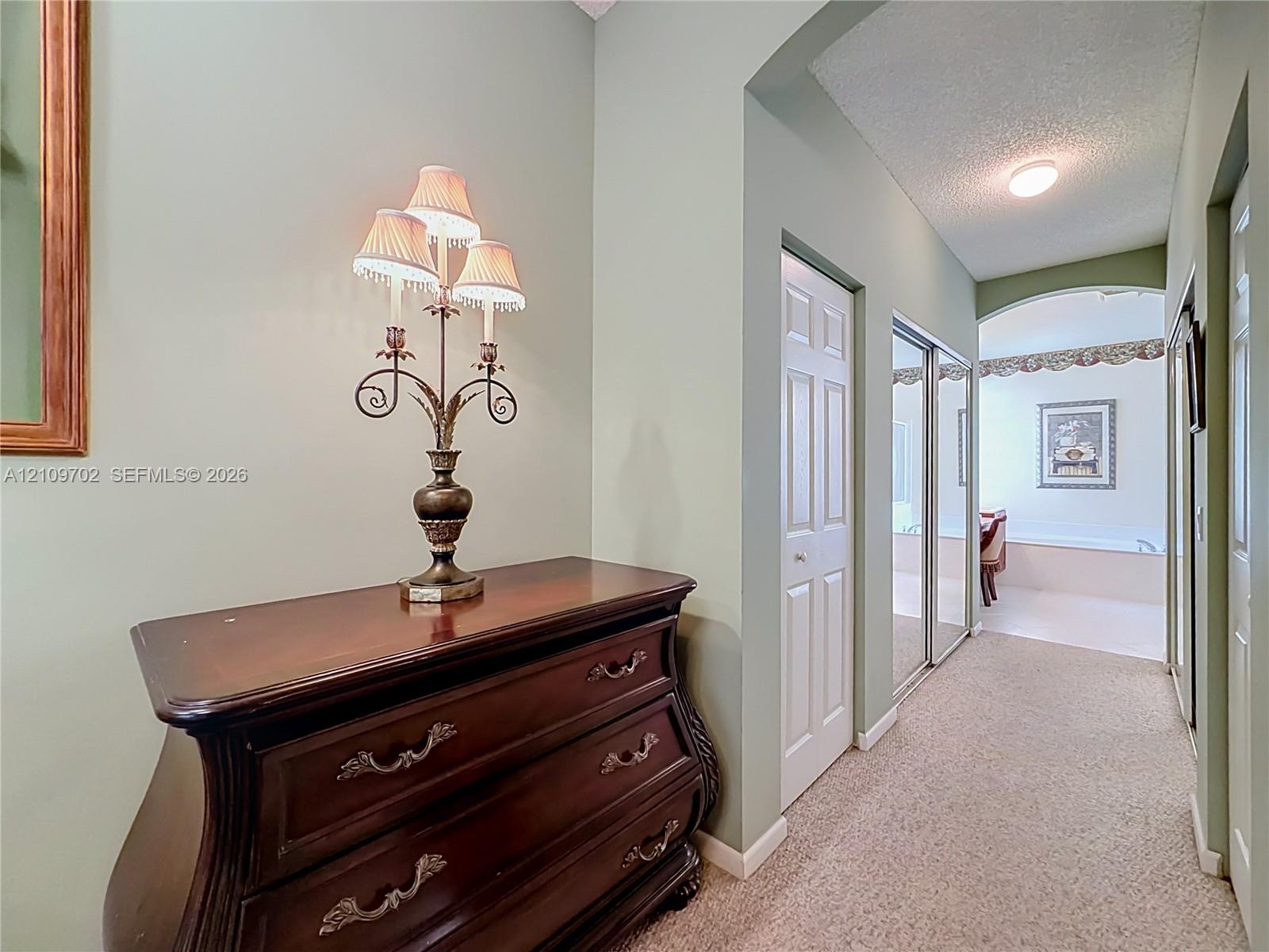 Hallway featuring arched architectural detailing, carpeted flooring, and mirrored closet doors
