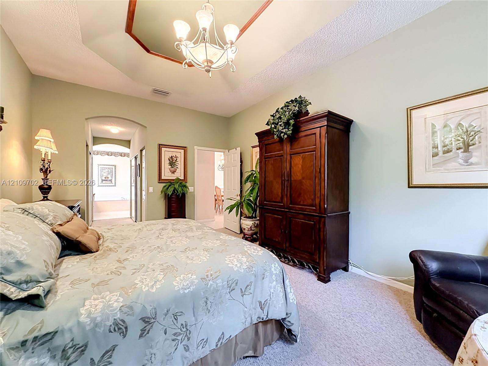 Tray ceiling with a decorative center feature, tiered chandelier, and arched doorway