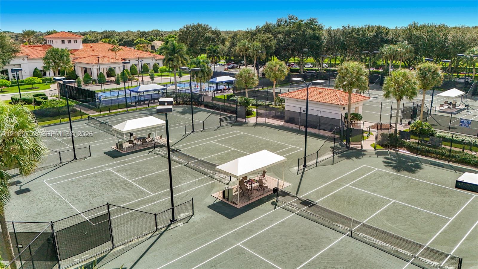 Multiple tennis courts featuring perimeter fencing, stadium-style lighting, and covered sideline seating areas