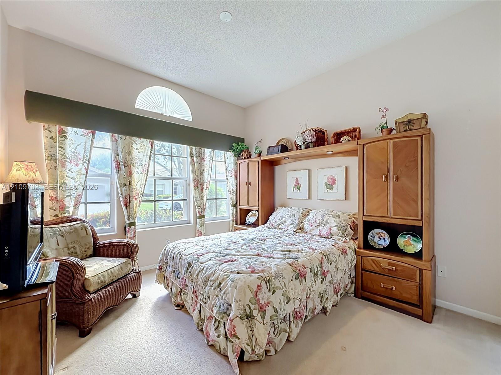 Room featuring high ceilings, neutral carpeted flooring, large windows, and a semi-circular transom window