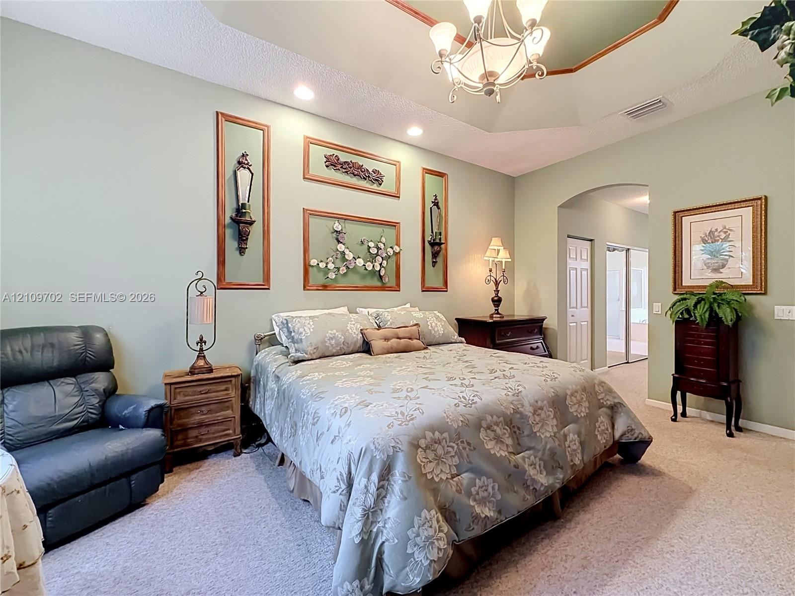 Tray ceiling featuring an integrated multi-light chandelier, arched entryway, and neutral wall-to-wall carpeting