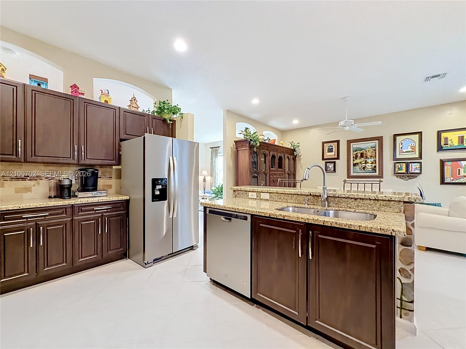 Kitchen featuring dark-finish cabinetry, stone-style countertops, stainless steel appliances, a dual-basin undermount sink, and tile flooring