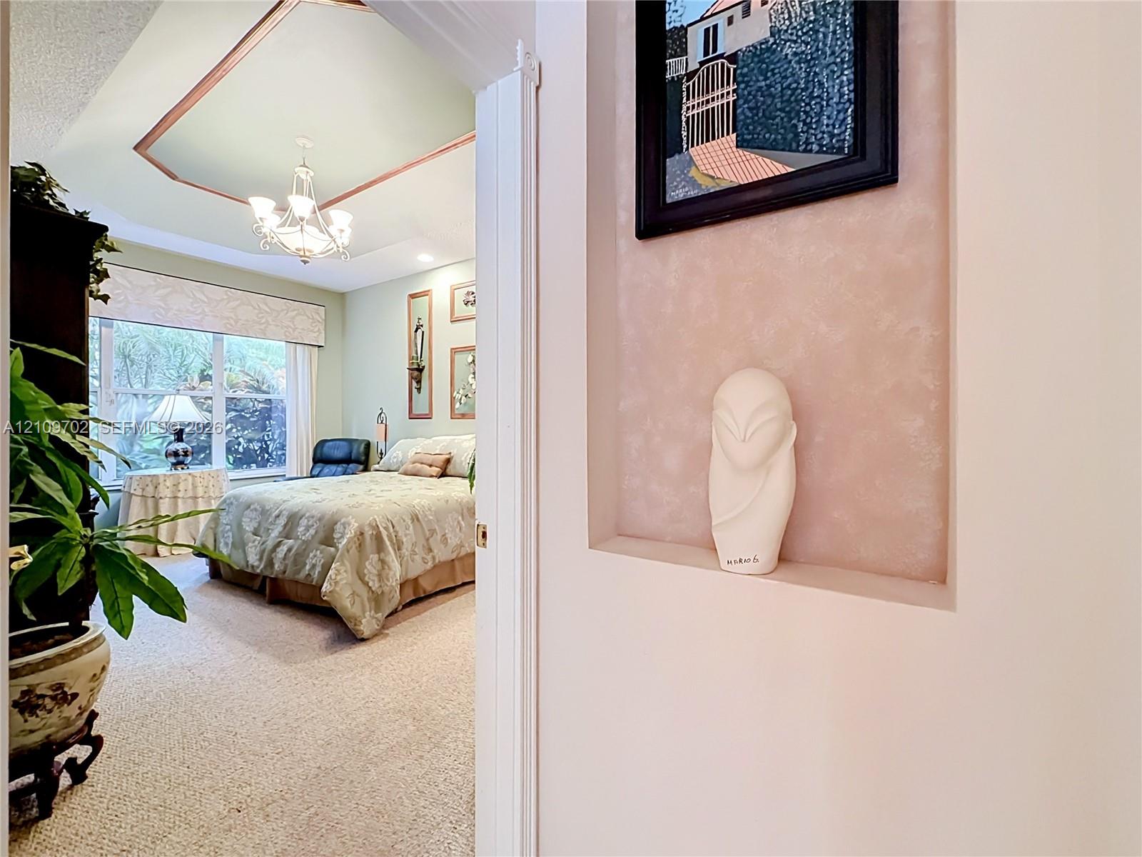 Recessed wall niche, tray ceiling with decorative trim, and multi-arm chandelier fixture