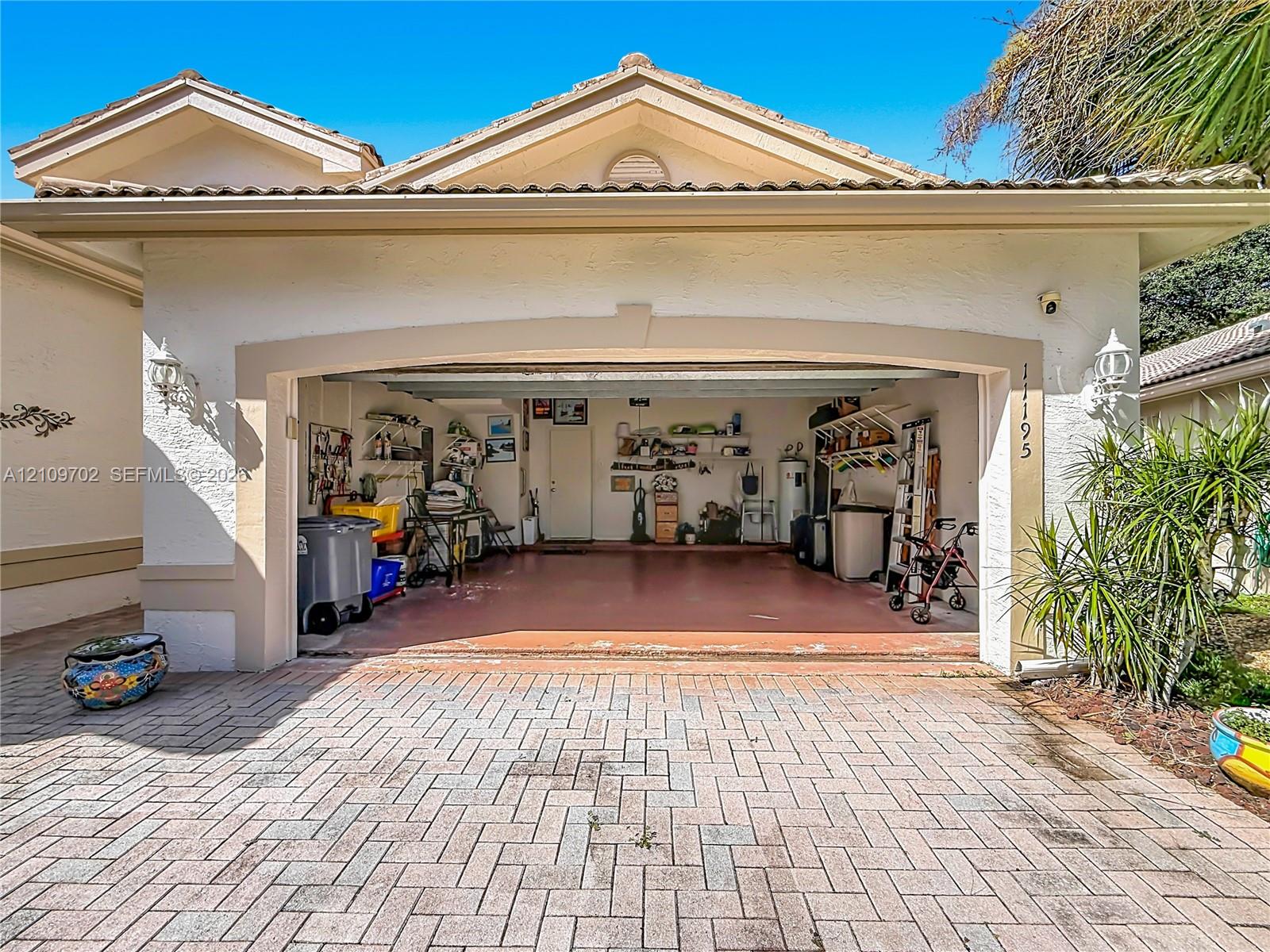 Stucco exterior featuring a dual-pitch roofline, paver driveway, and wall-mounted exterior light fixtures
