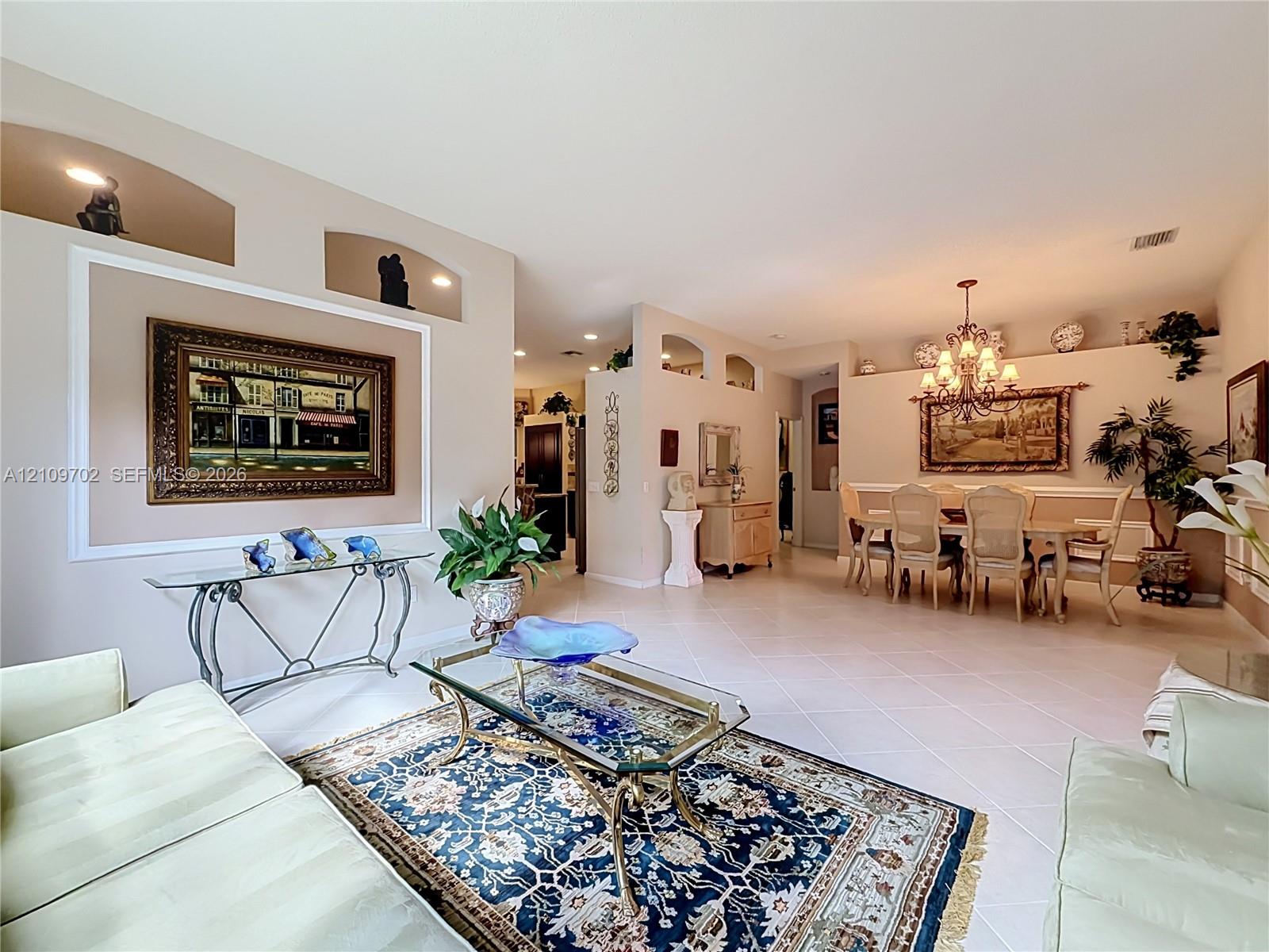 Open-concept interior featuring high ceilings, decorative wall niches, ceramic tile flooring, and an ornate chandelier