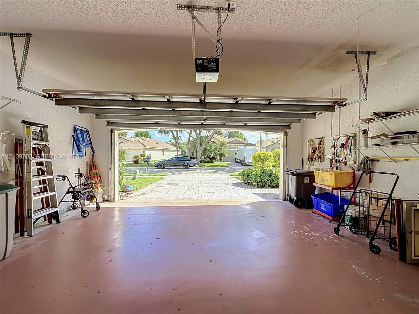 Two-car garage featuring an automated overhead door opener, concrete flooring, and built-in wall-mounted shelving