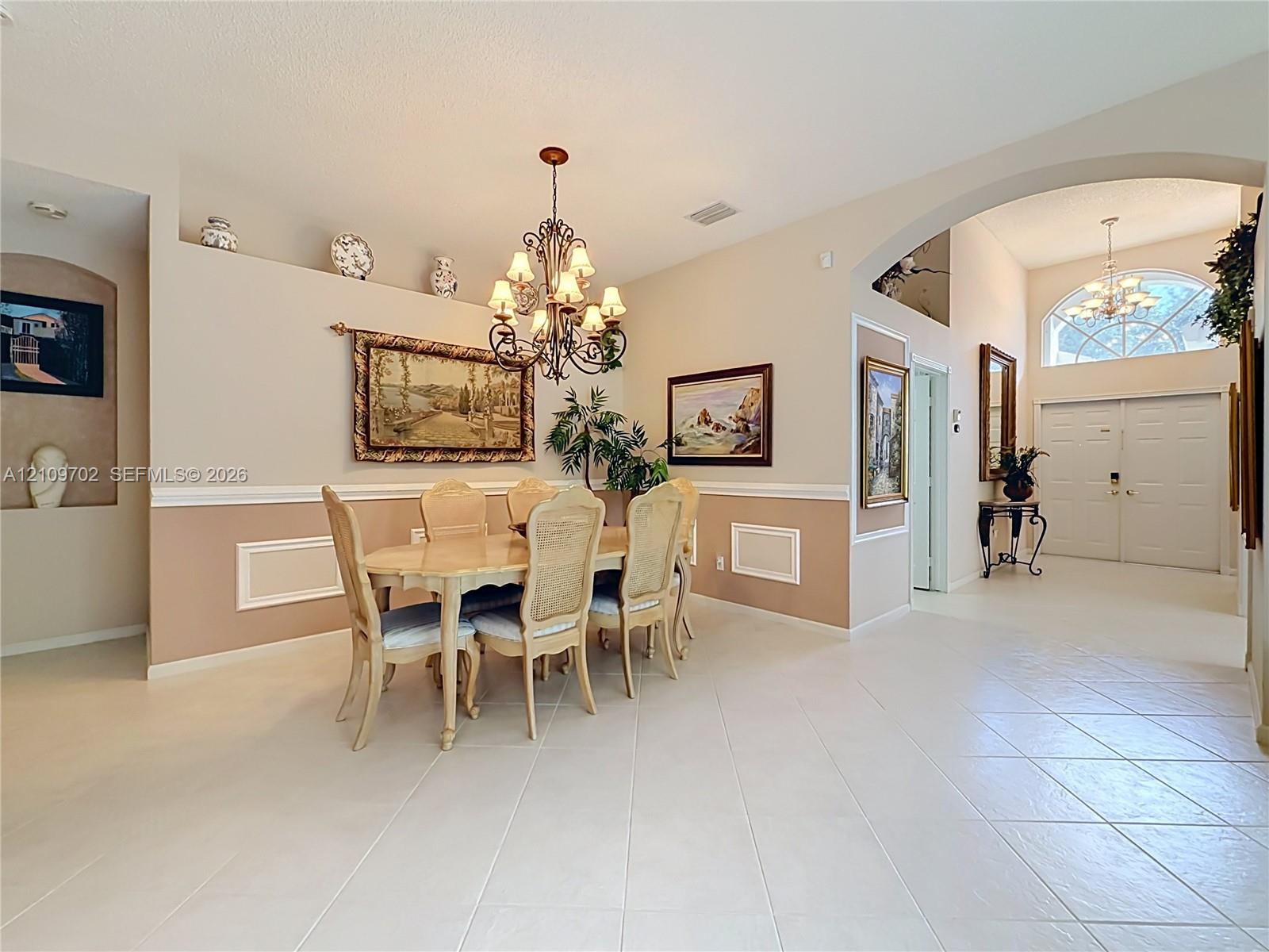 Interior area featuring ceramic tile flooring, arched entryways, decorative wall niches, chair rail molding, and a multi-arm chandelier