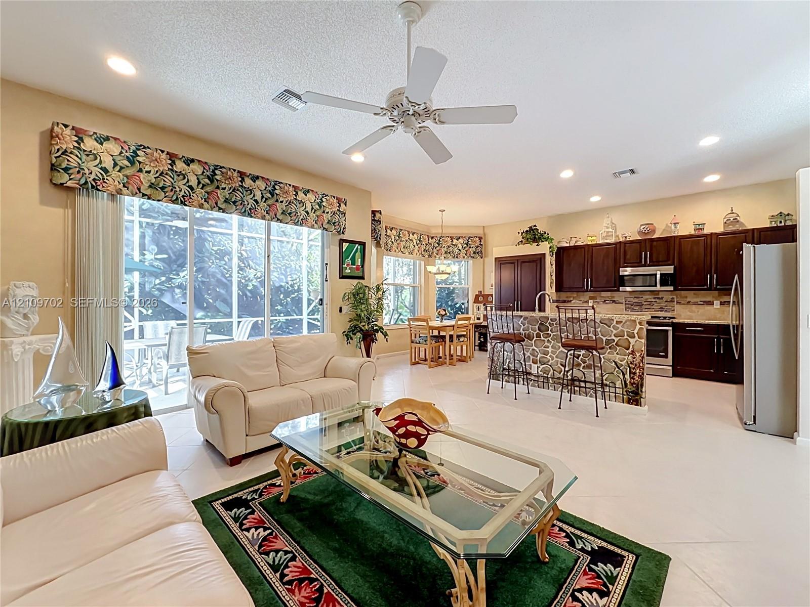 Open-concept layout featuring recessed lighting, a stone-accented breakfast bar, dark-finish cabinetry, tile flooring, and large sliding glass doors