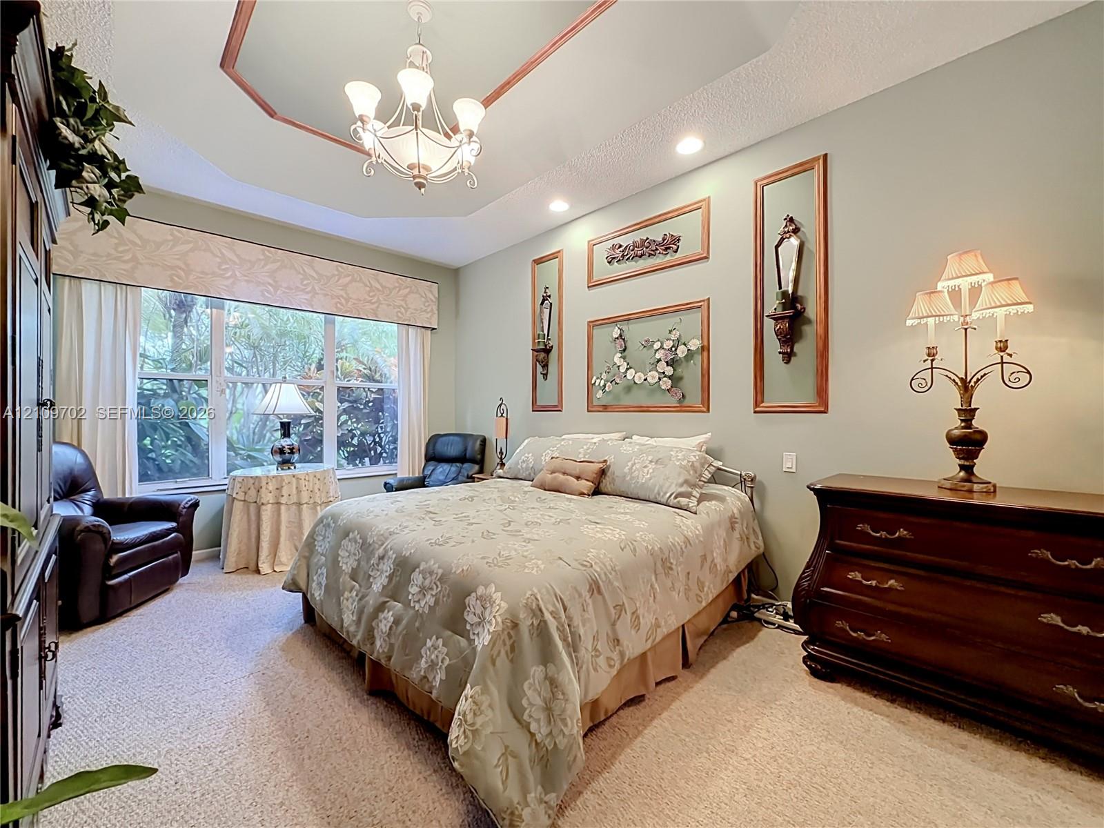 Tray ceiling with crown molding, multi-light chandelier, recessed lighting, and large window with built-in custom valance