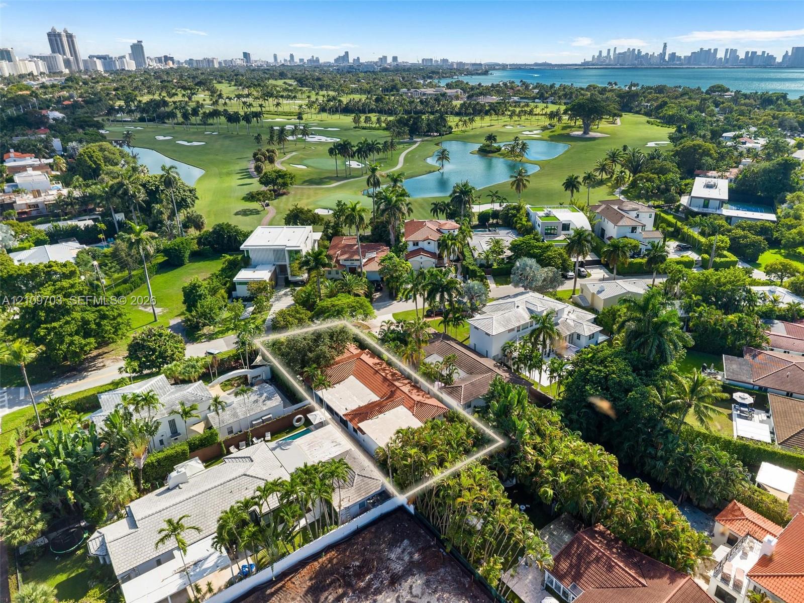 Aerial perspective highlighting a property with a clay tile roof, mature perimeter landscaping, and proximity to a golf course, water bodies, and coastal city skyline