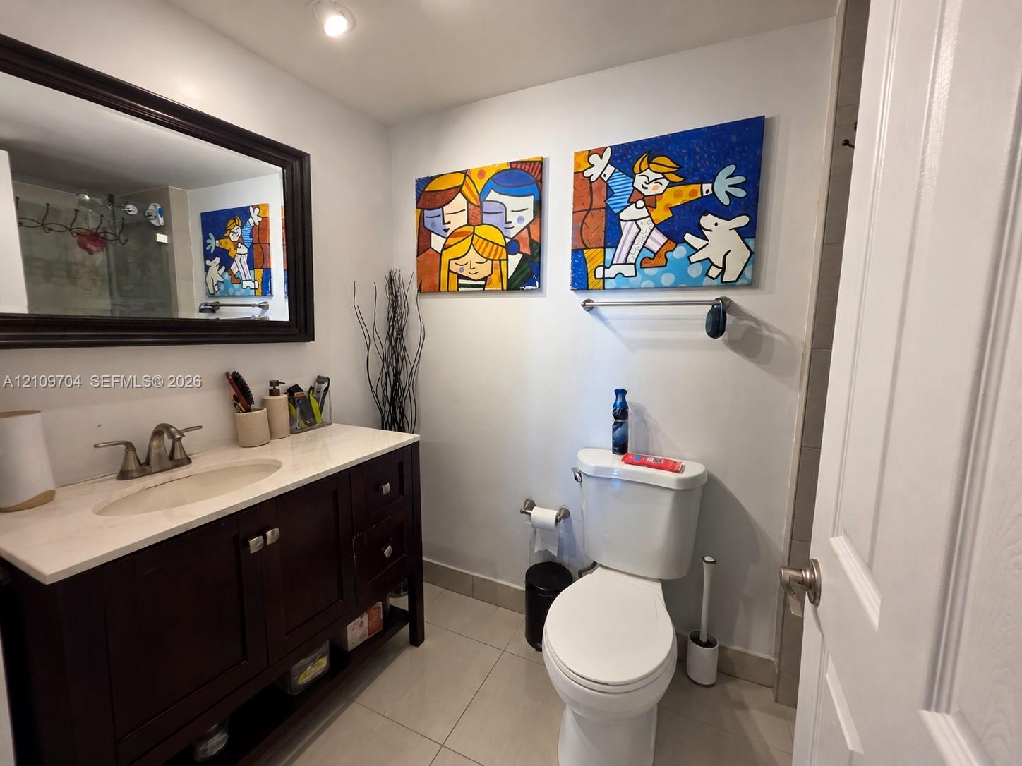 Bathroom featuring a dark-finish wood vanity, integrated sink with a metallic faucet, stone-composite countertop, large framed wall mirror, and neutral tile flooring