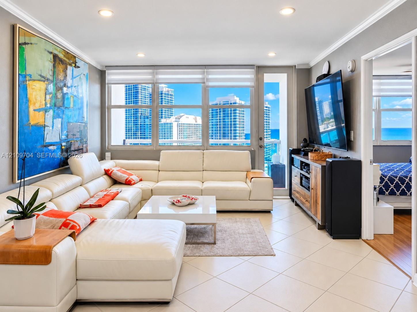 Living area featuring large format tile flooring, recessed ceiling lighting, and floor-to-ceiling windows with panoramic city and coastal scenery
