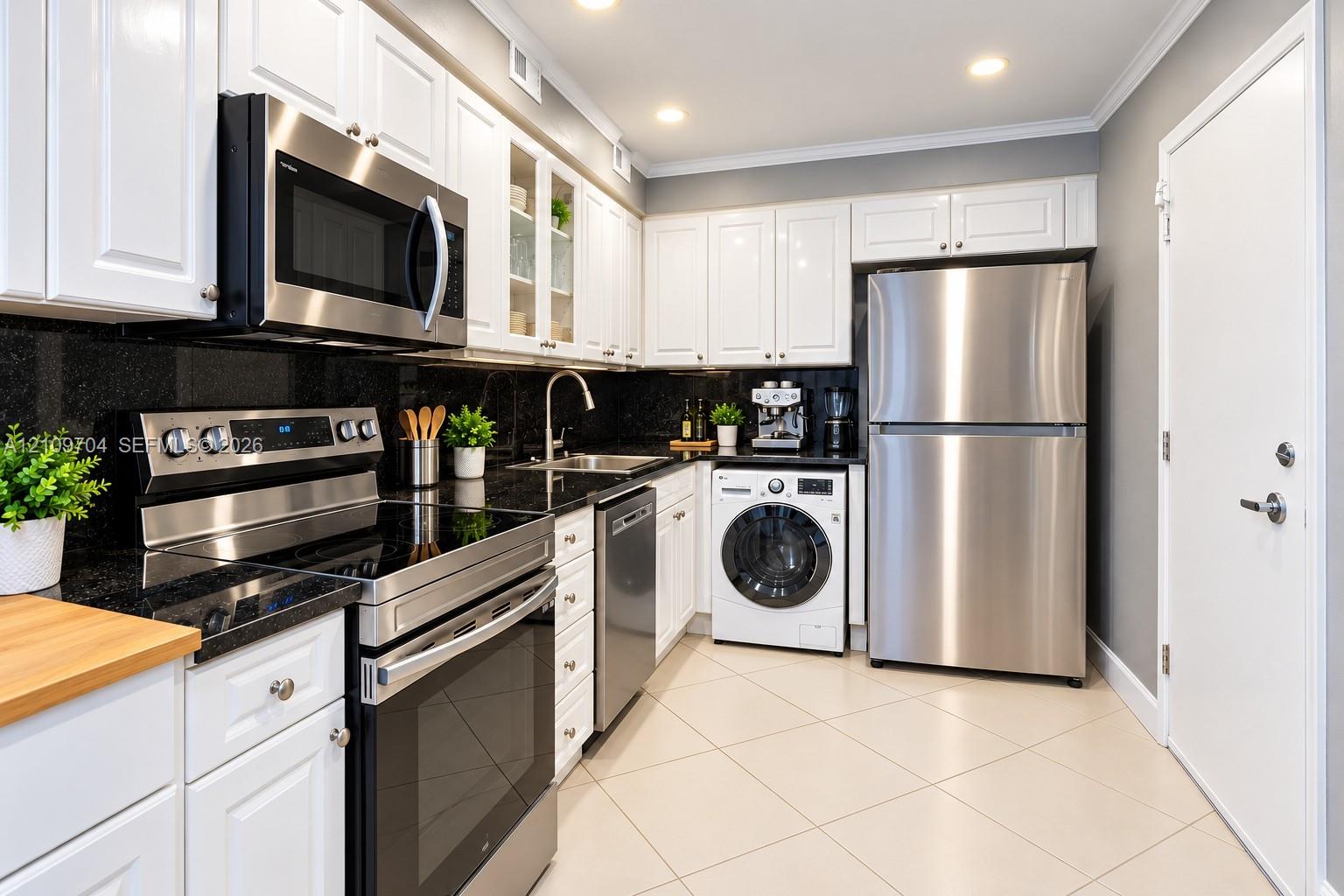 Kitchen featuring white shaker-style cabinetry, dark stone countertops, stainless steel appliances, integrated laundry, and light-toned tile flooring