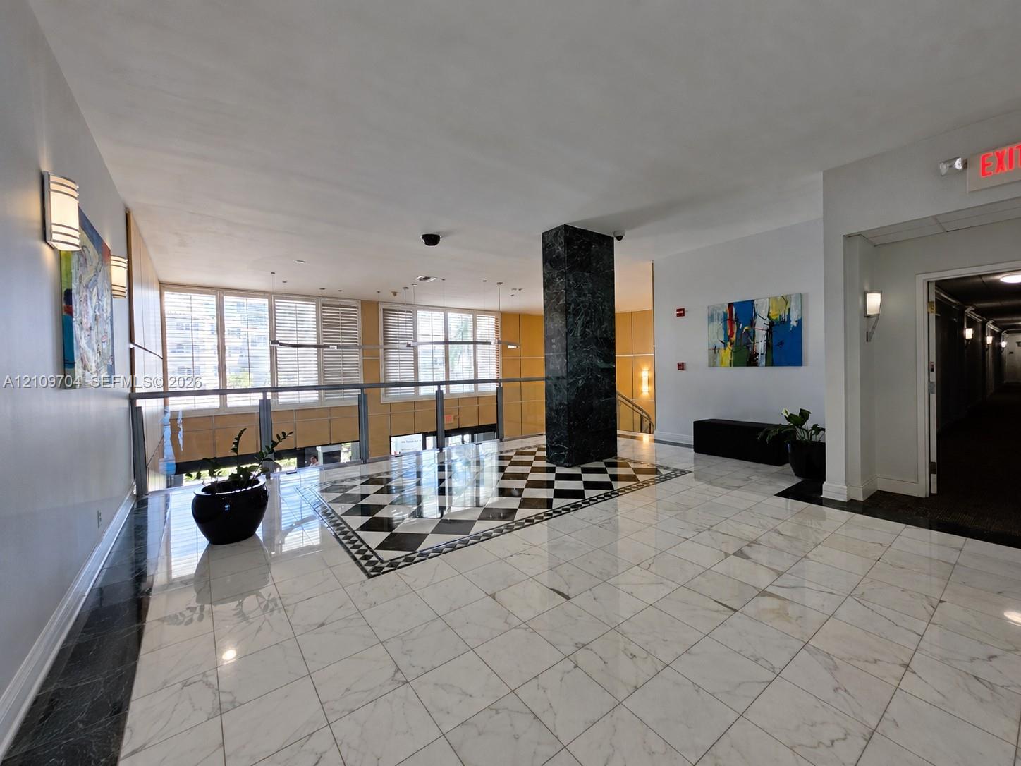 Lobby entrance featuring stone tile flooring with a checkered inset, a central dark stone-clad pillar, and multi-pane windows with integrated shutters