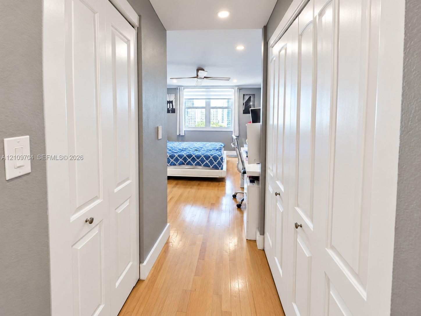 Hallway featuring wood-finish flooring, recessed lighting, and dual sets of white bi-fold closet doors