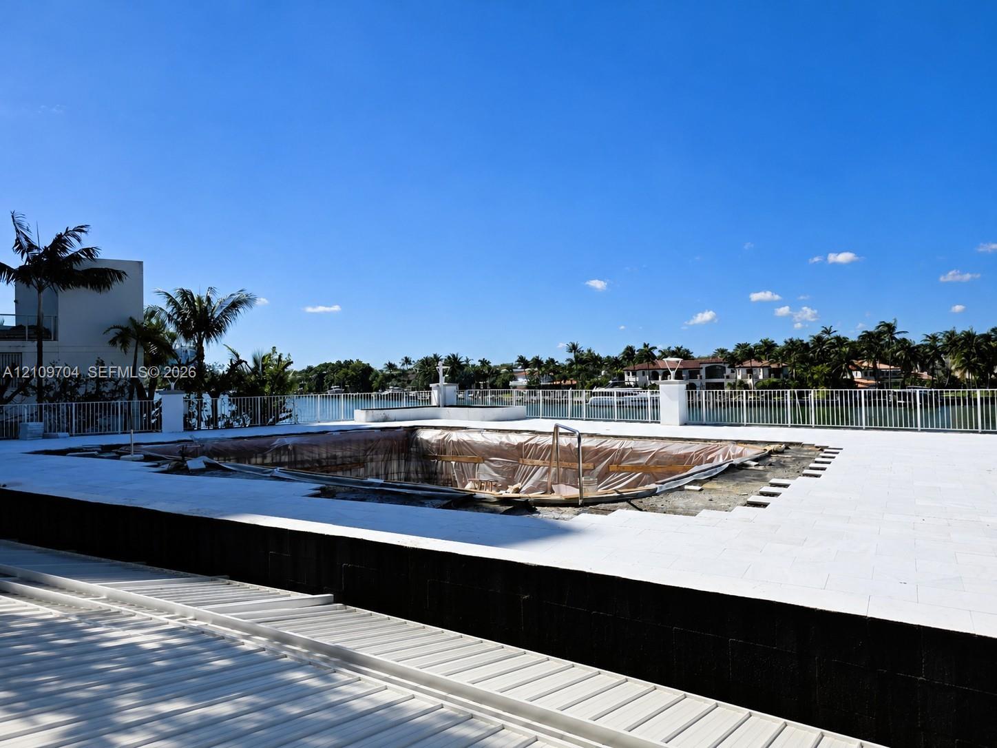 Waterfront terrace featuring a tiled deck, perimeter metal fencing, and a pool basin under construction