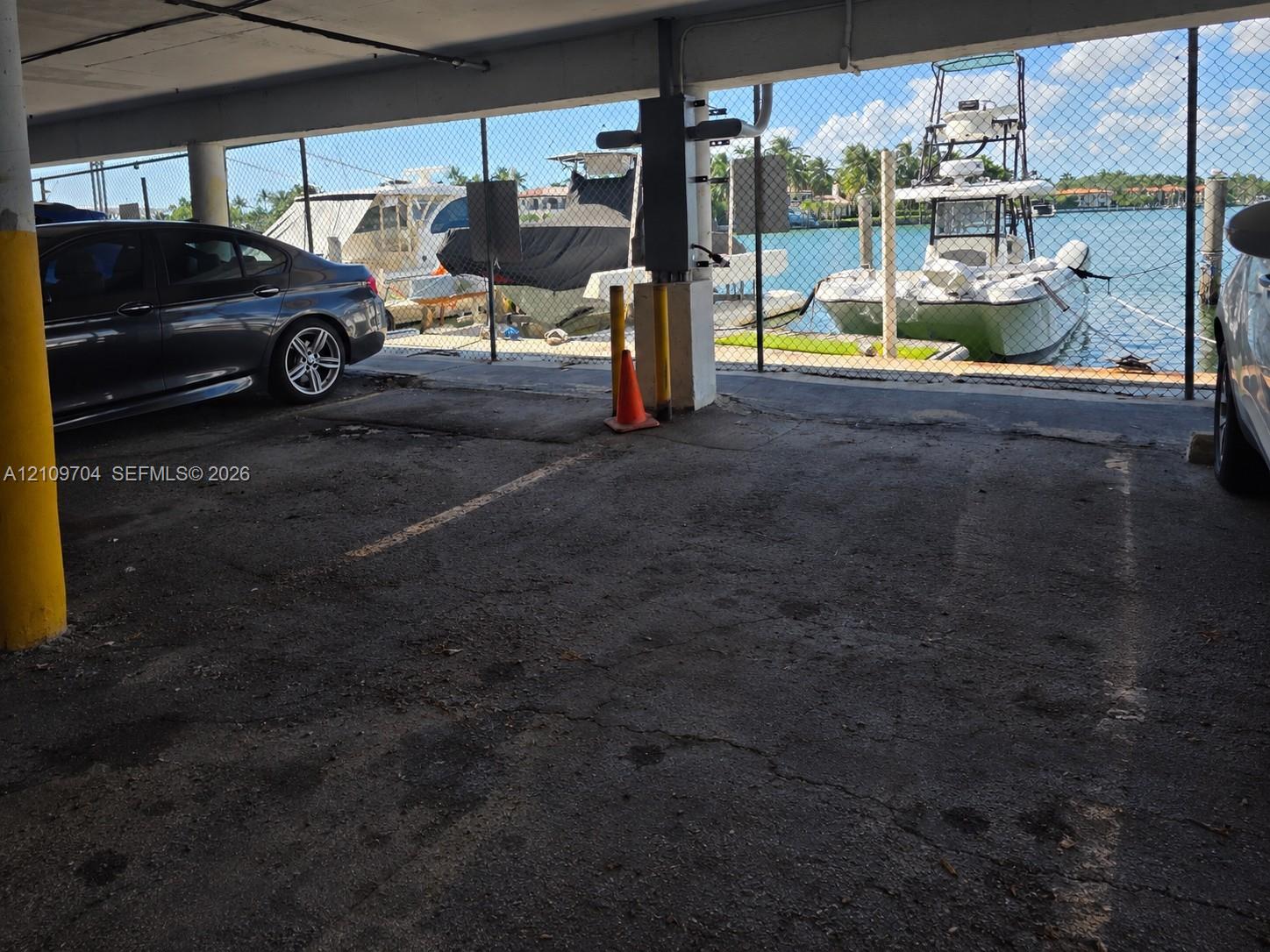 Covered parking space featuring asphalt paving, concrete support pillars, and direct proximity to a canal-side dock