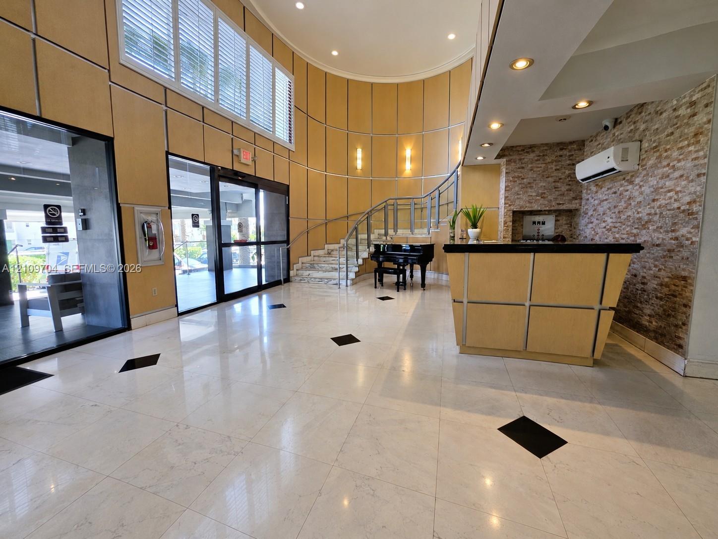 Polished tile flooring with geometric inlays, curved wall paneling, stone veneer accent wall, glass and metal staircase railing, and recessed ceiling lighting