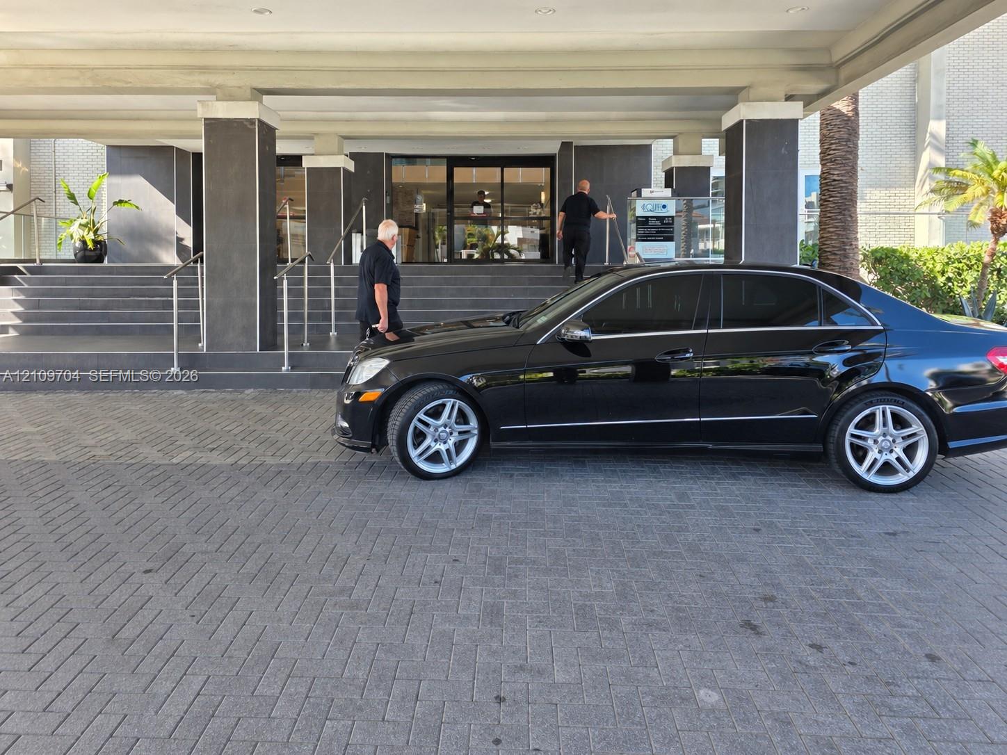 Covered drive-up entrance featuring a stone-paver motor court, concrete stairs, and glass-entry doors with metallic handrails