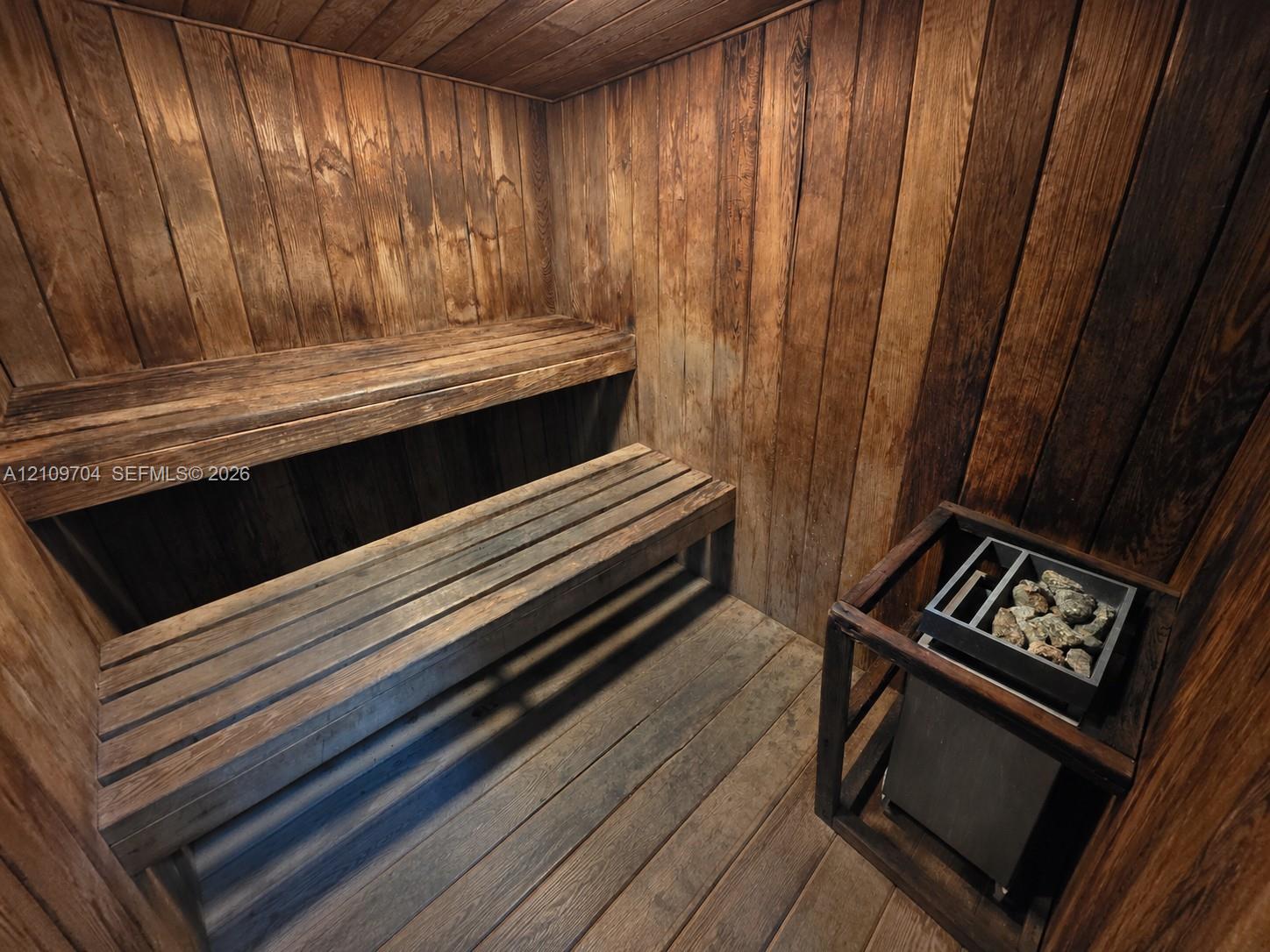 Custom sauna featuring tongue-and-groove wood paneling, multi-level slatted wood benches, and a built-in electric rock heater