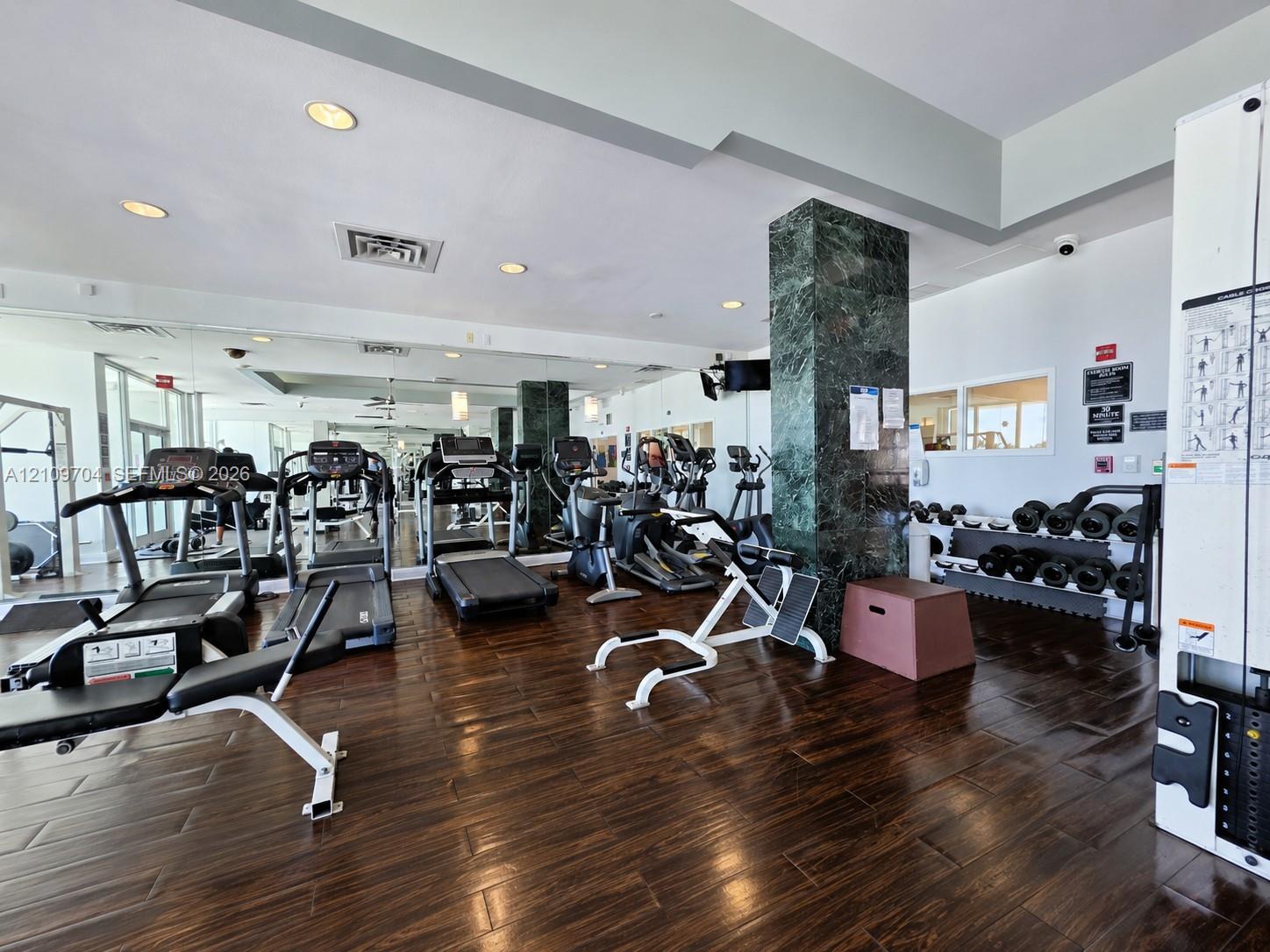 Fitness center featuring wood-finish flooring, floor-to-ceiling mirrored walls, and a decorative stone-clad structural column